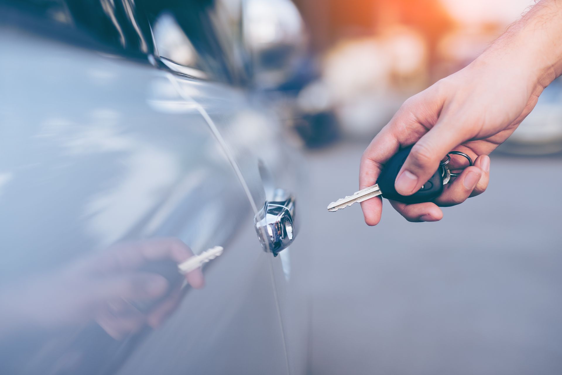 A person is holding a car key in front of a car.