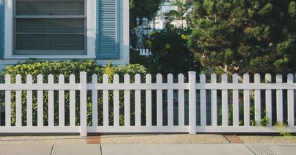 A white picket fence surrounds a house with blue shutters