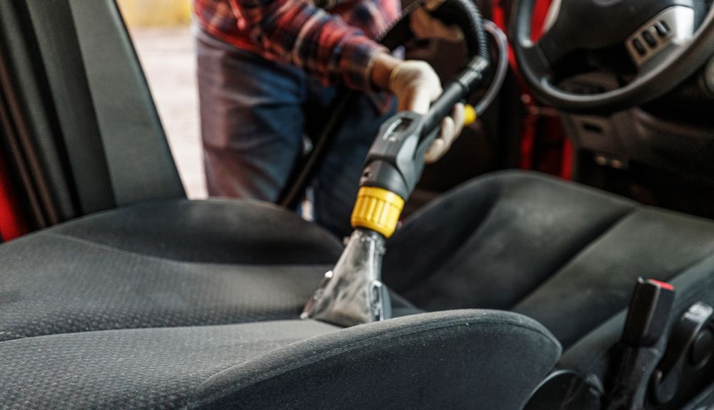 A man is cleaning the seats of a car with a vacuum cleaner.