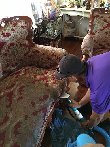 A man is cleaning a couch with a vacuum cleaner.