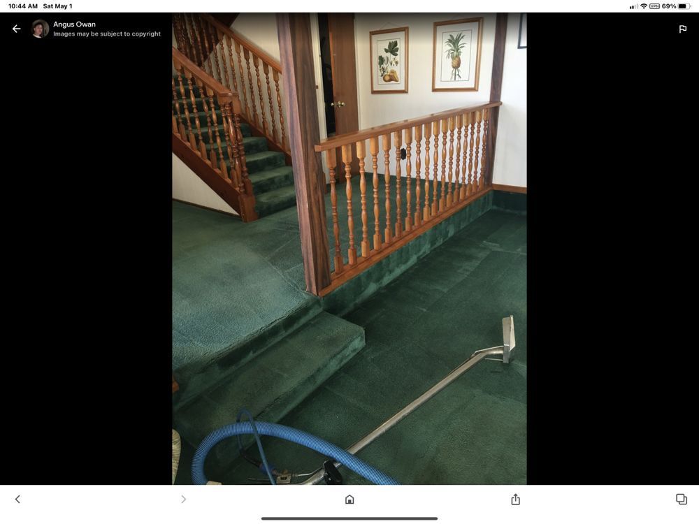 A picture of a staircase with green carpet and a vacuum cleaner.
