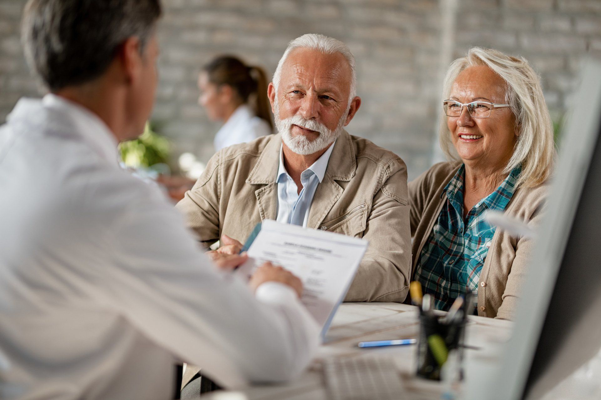 An elderly couple is sitting at a table talking to a doctor.