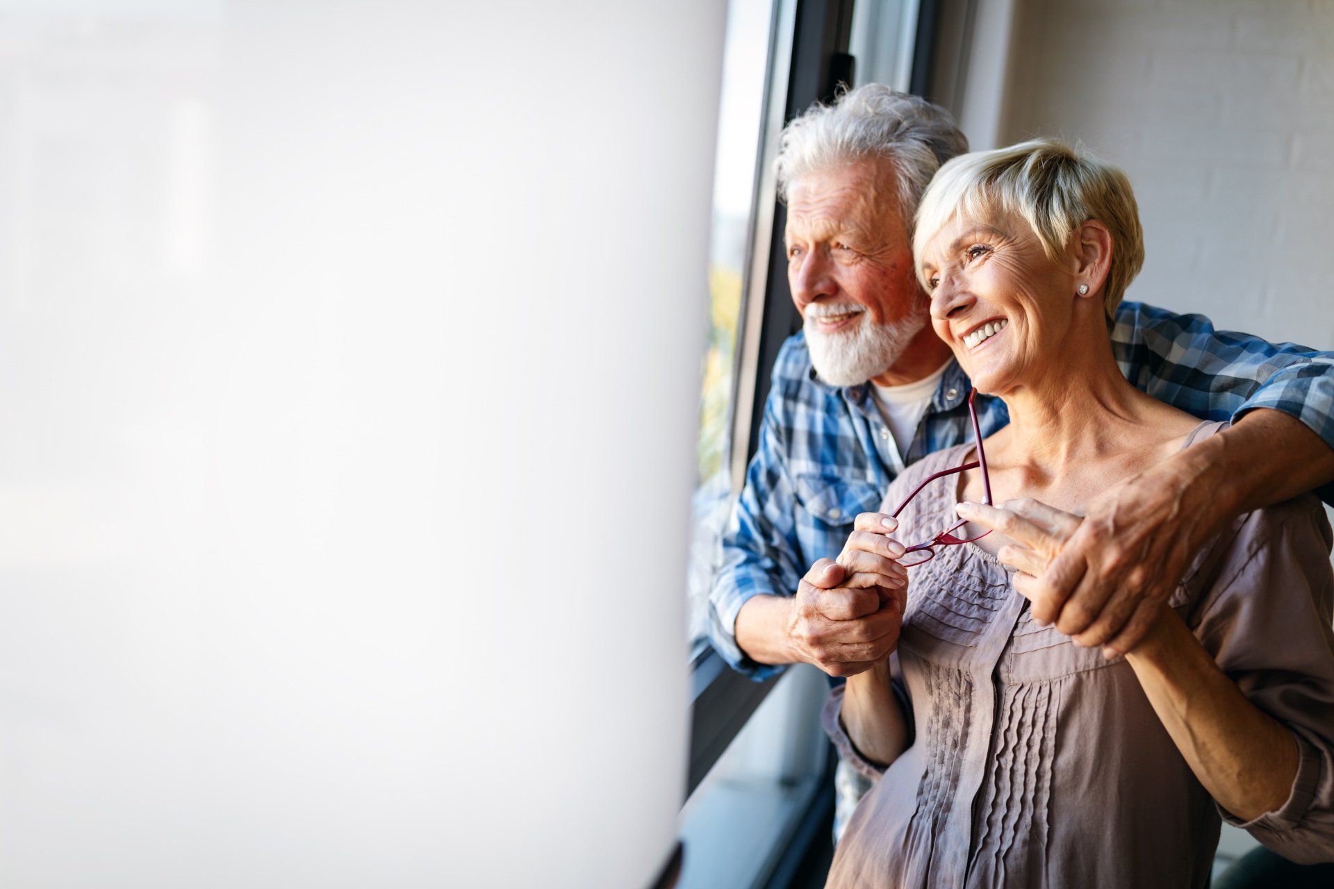 An elderly couple is looking out of a window.