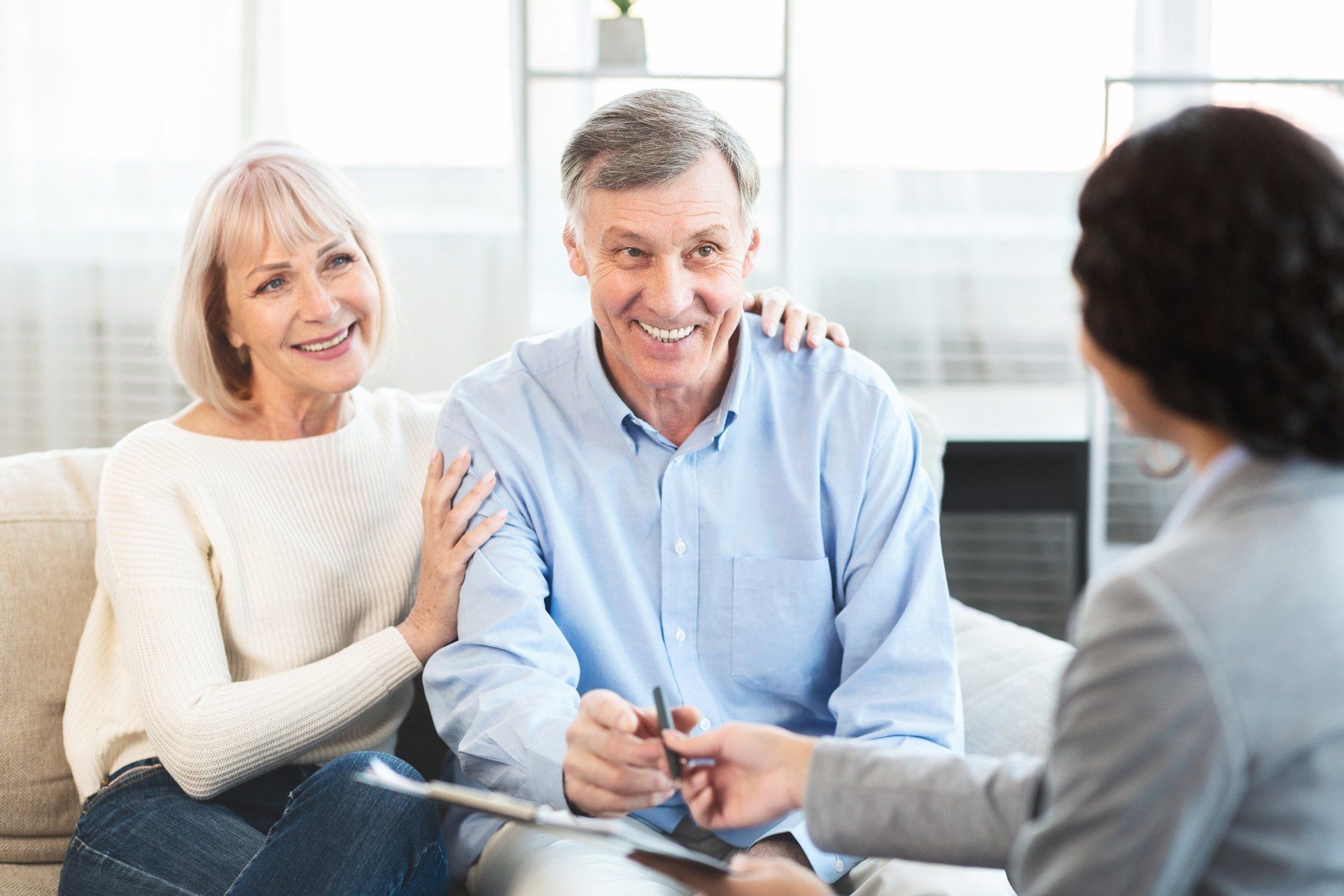 An elderly couple is sitting on a couch talking to a woman.