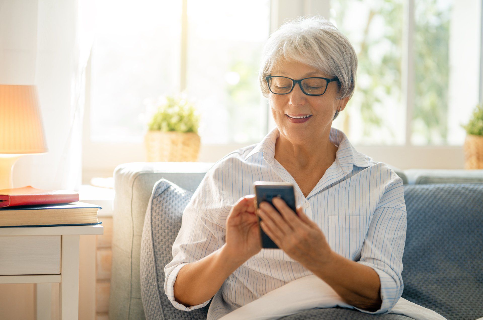 An elderly woman is sitting on a couch using a cell phone.