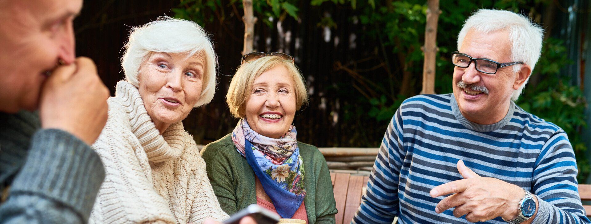 A group of elderly people are sitting on a bench talking to each other.