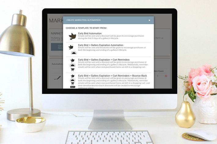 Computer monitor displaying a pop-up menu with text and icons, on a desk with a lamp and flowers.
