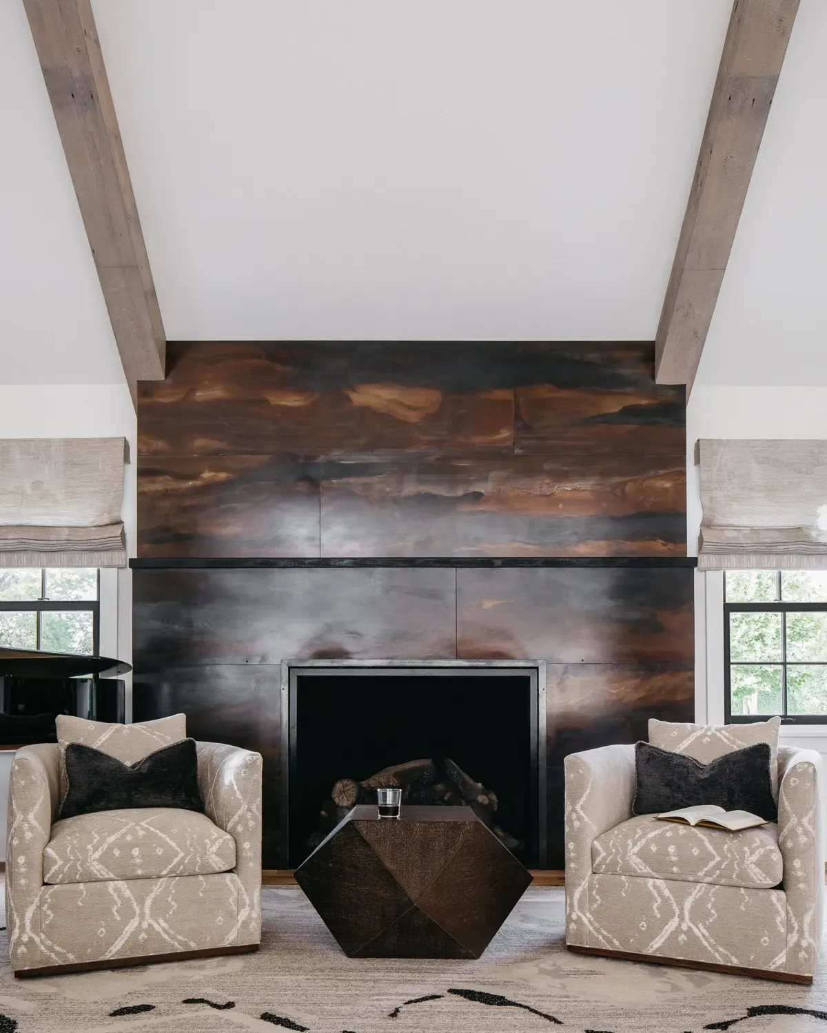 A living room with two chairs and a fireplace with reclaimed beams along either side.