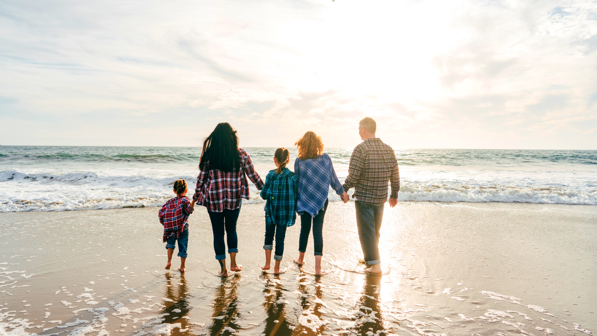 A family is walking on the beach holding hands.