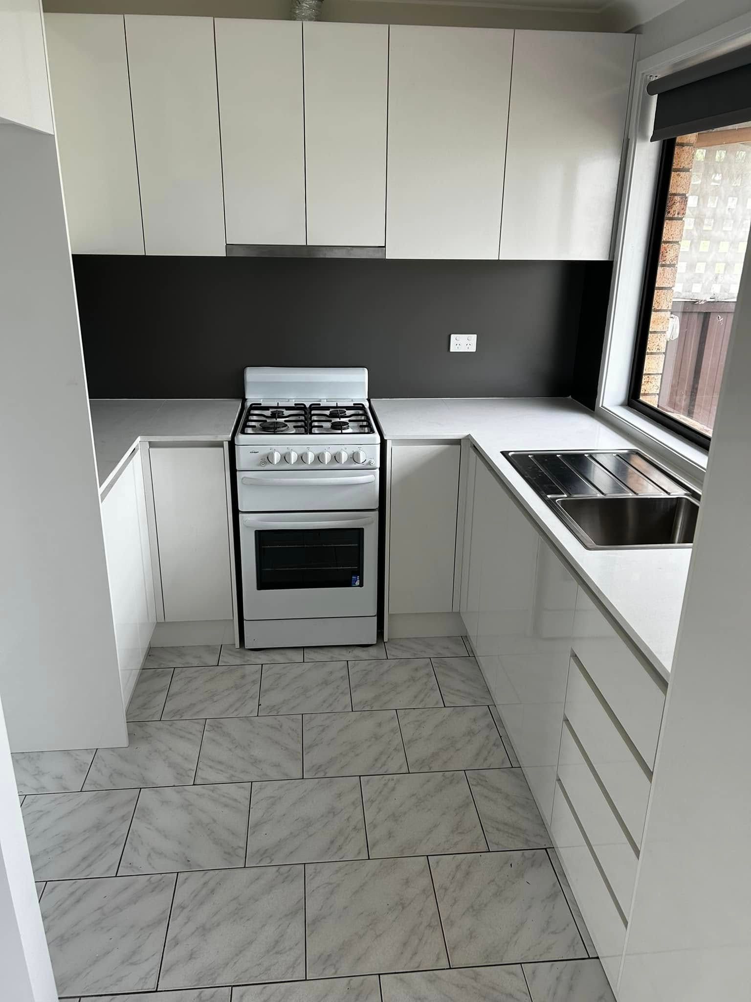 White Kitchen With Stove, Sink, Cabinets, Grey Backsplash, And Tiled Floor — Protech Renovations & Joinery in Wollongong, NSW
