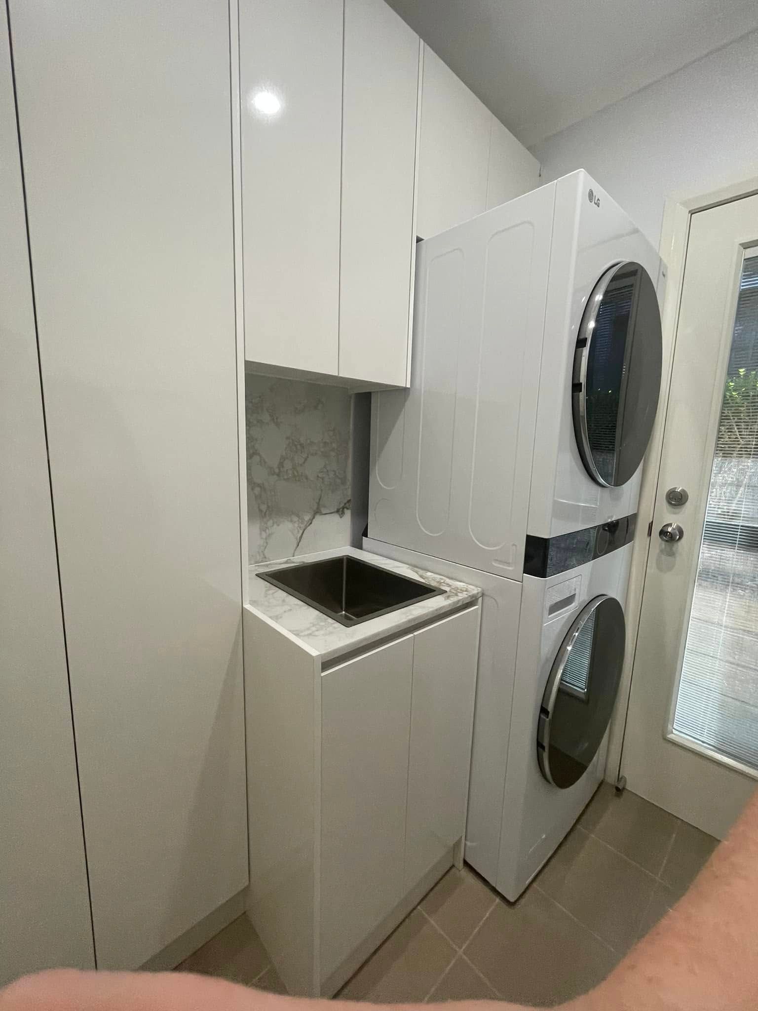Laundry Room With White Cabinets, Stacked Washer/Dryer, And Sink — Protech Renovations & Joinery in Narellan, NSW
