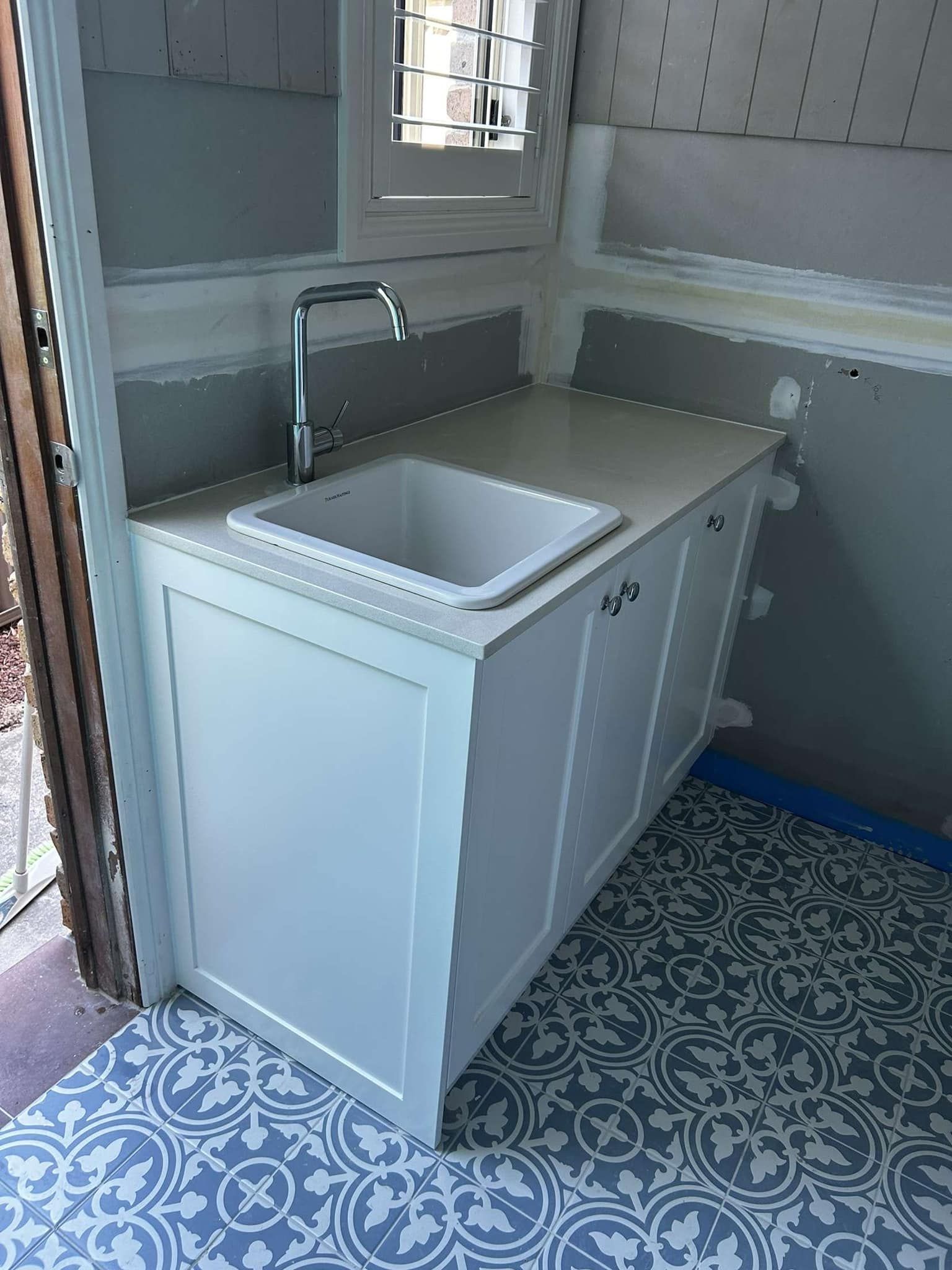 White Sink And Cabinets In Small Room With Patterned Blue Floor Tiles — Protech Renovations & Joinery in Camden, NSW