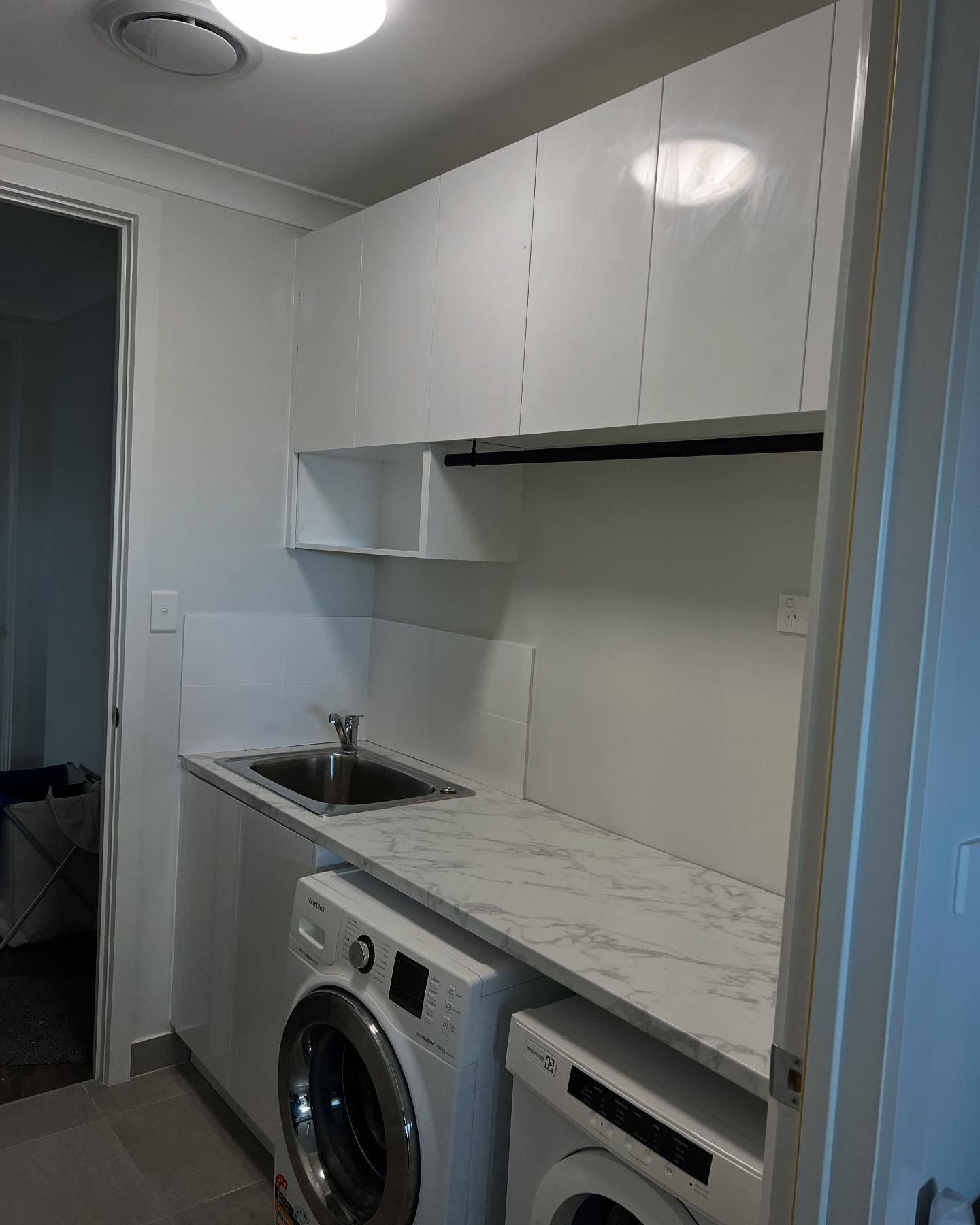 Laundry room with stacked white washer/dryer, sink, and white cabinets. — Protech Renovations & Joinery in Gregory Hills, NSW