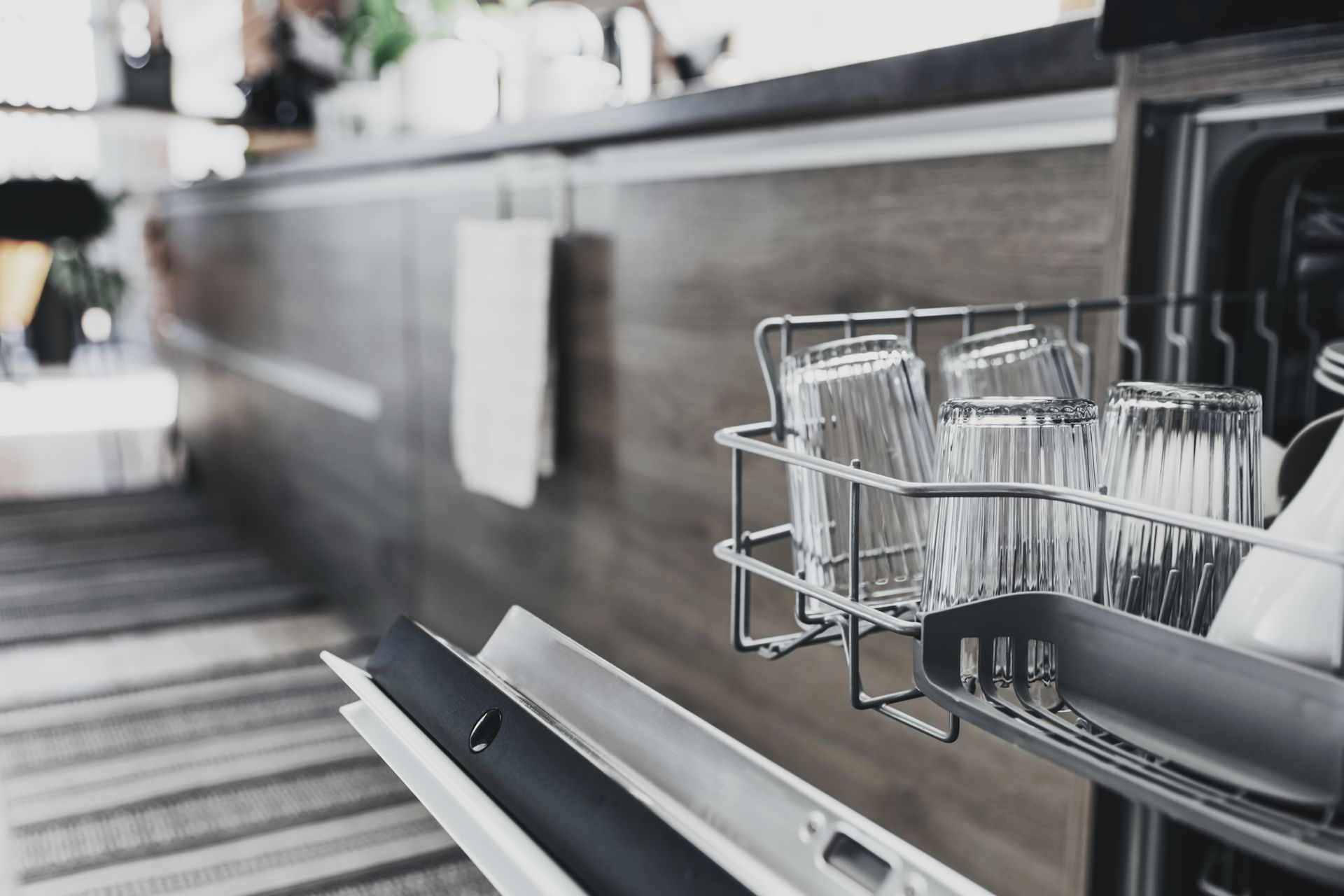 A man is kneeling down in front of a dishwasher in a kitchen.