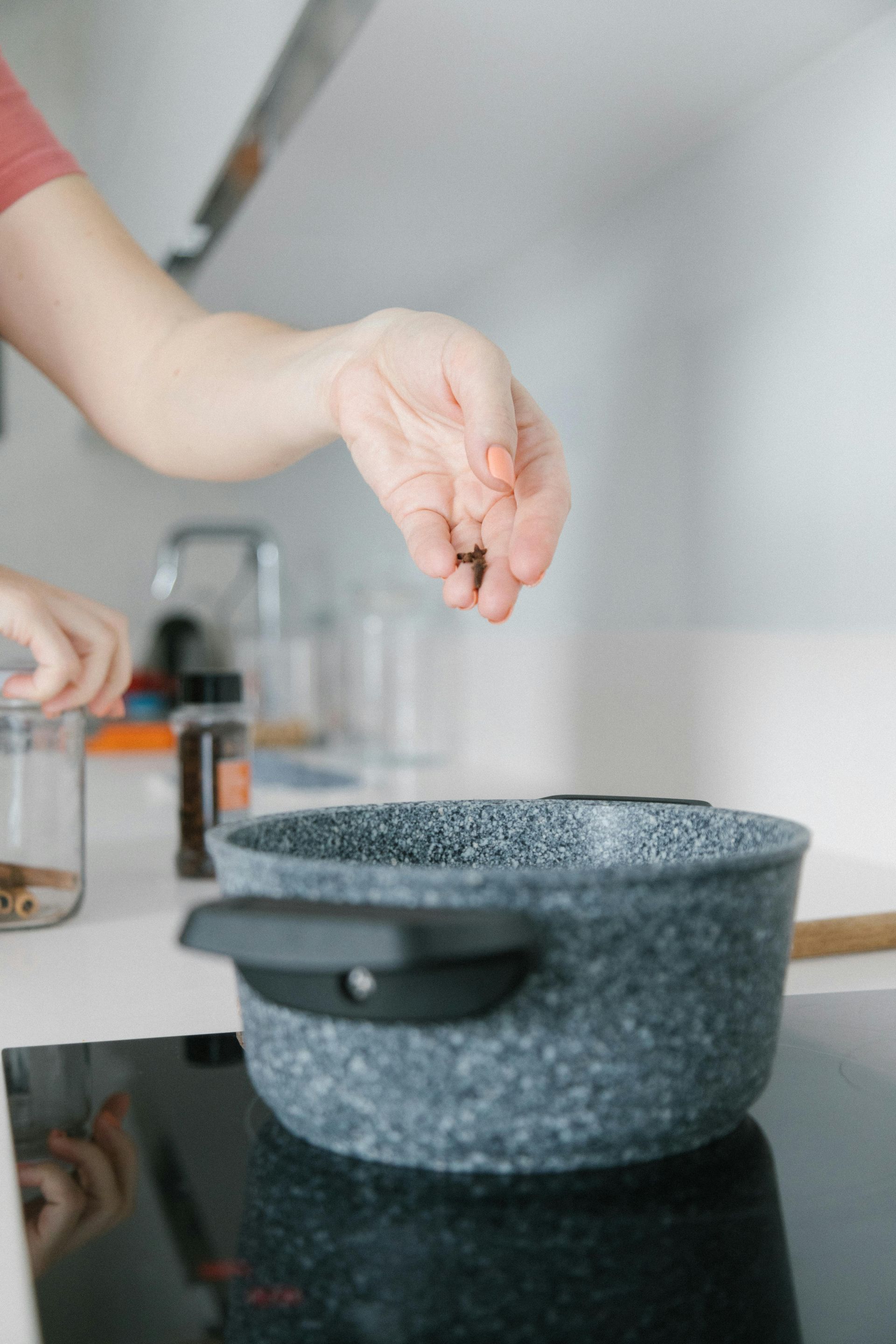 Person seasoning food in pot on glass cooktop surface in modern kitchen