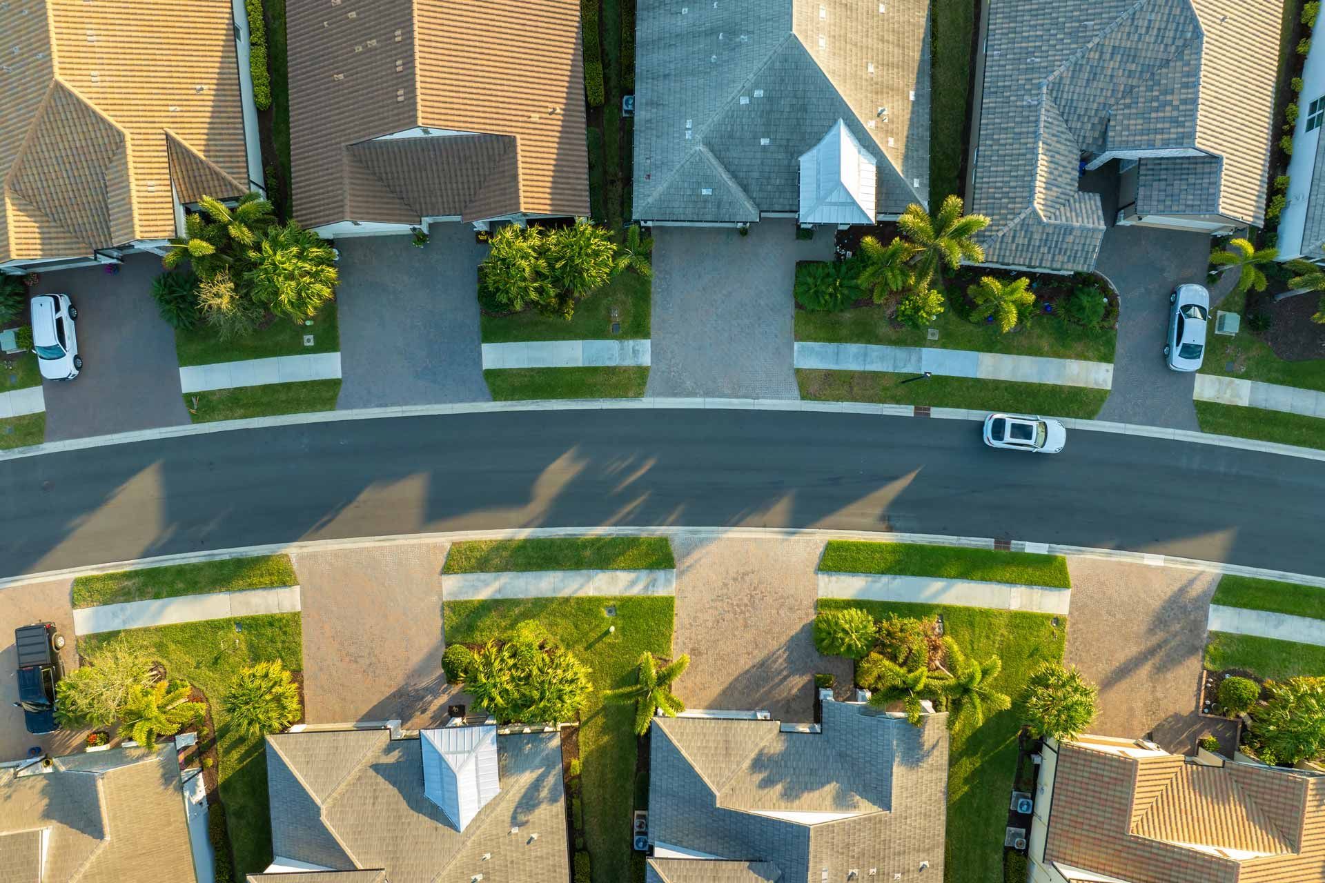 Aerial view of a suburban neighborhood with houses, driveways, green lawns, and a curved road.