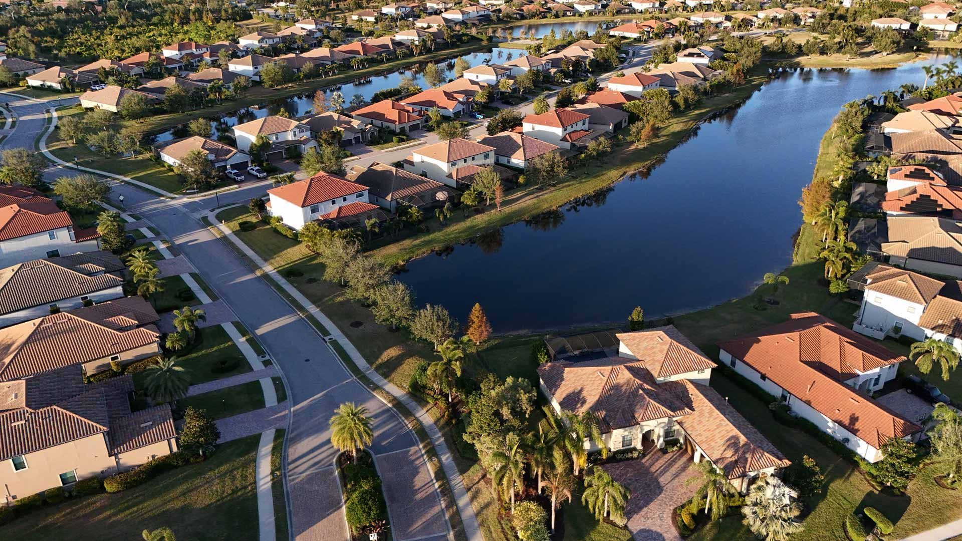 Beige stucco mansion with terracotta roof, framed by green trees and blue sky.