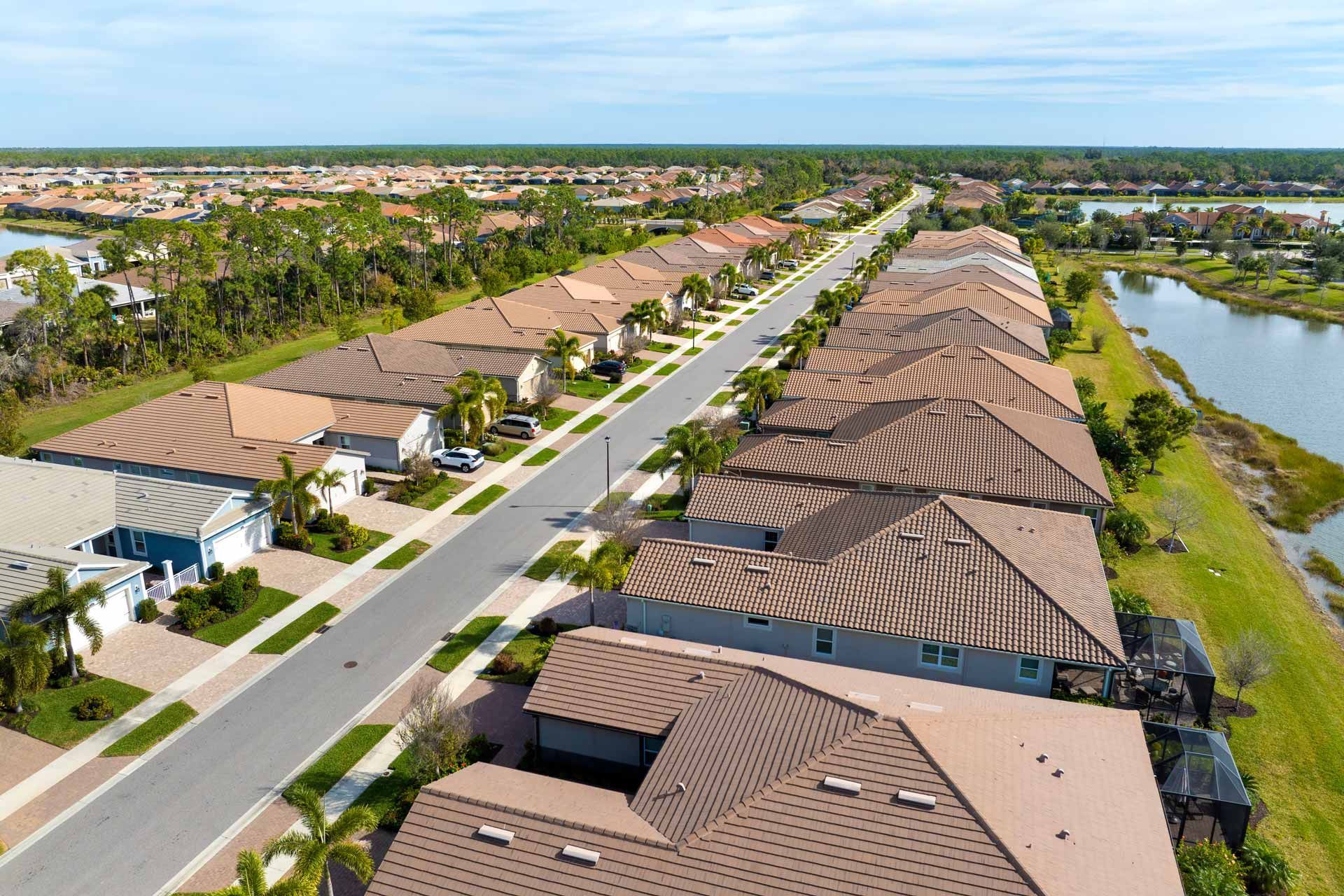 Aerial view of a suburban neighborhood with rows of houses, a road, and a lake under a blue sky.