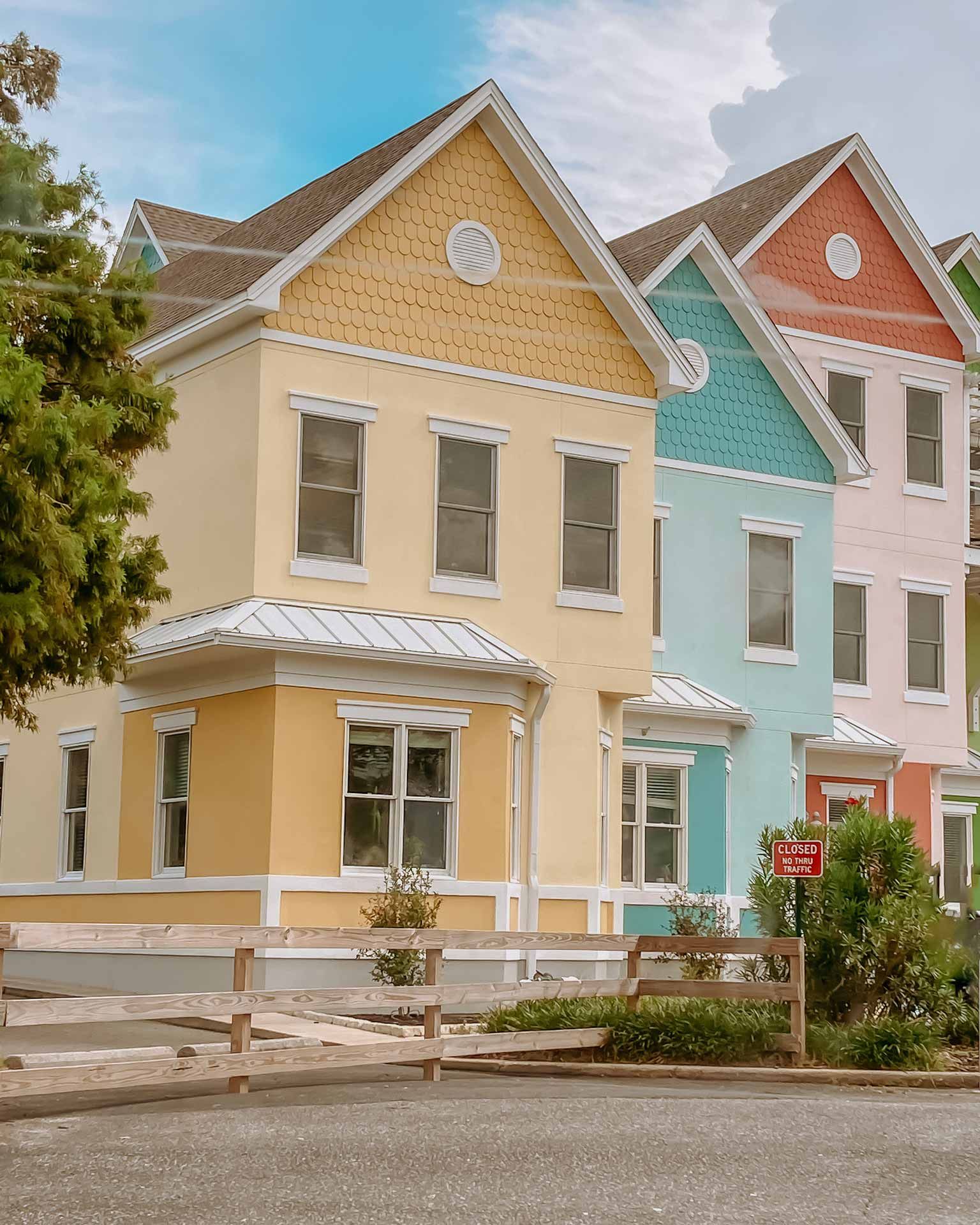 Row of colorful houses: yellow, blue, and pink with white trim, set in a neighborhood.