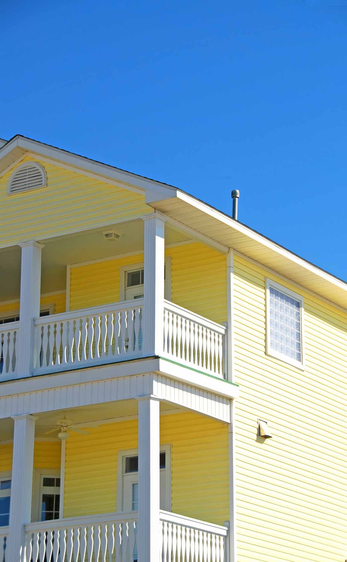 Yellow two-story building with white balconies against a bright blue sky.