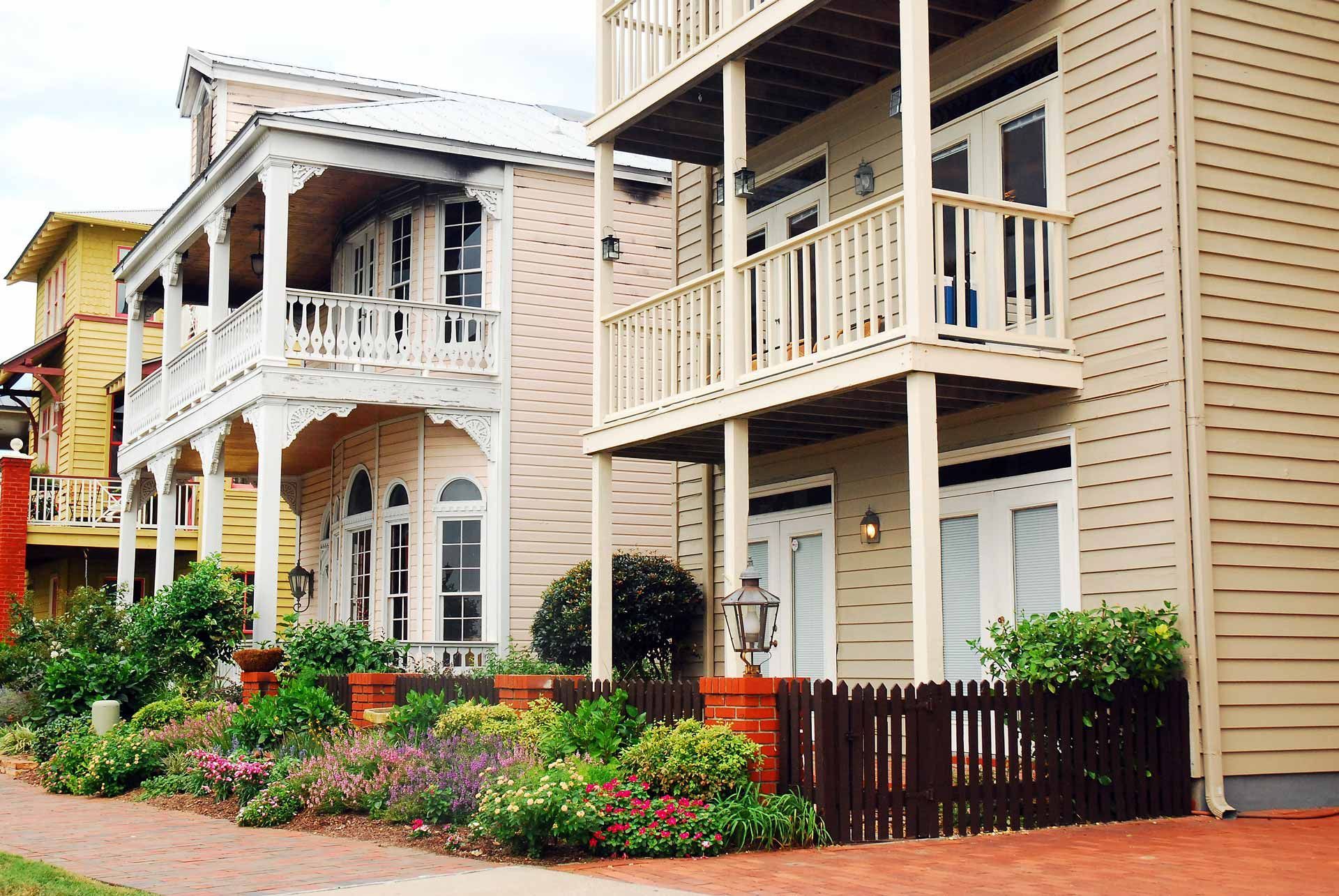 Multi-story buildings with balconies, light siding, a brick walkway, and a small garden.