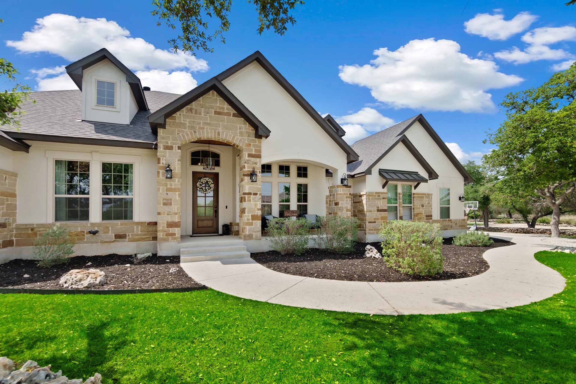 White stucco house with stone accents, lush green lawn, and winding walkway.