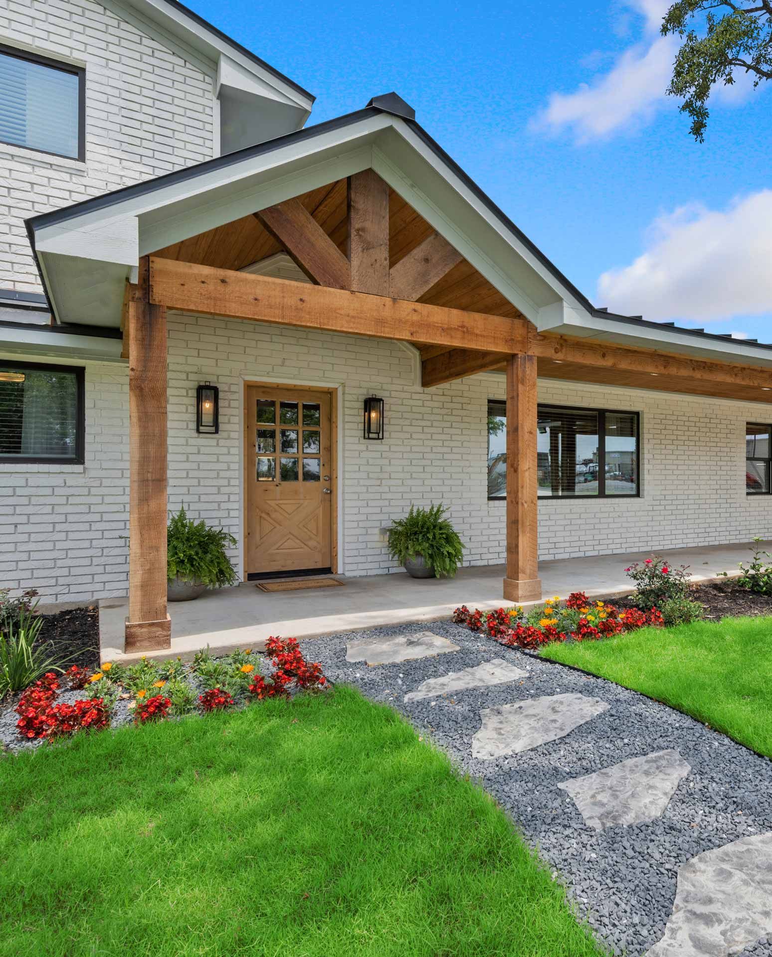 White brick house with wooden porch and stone pathway lined with flowers.