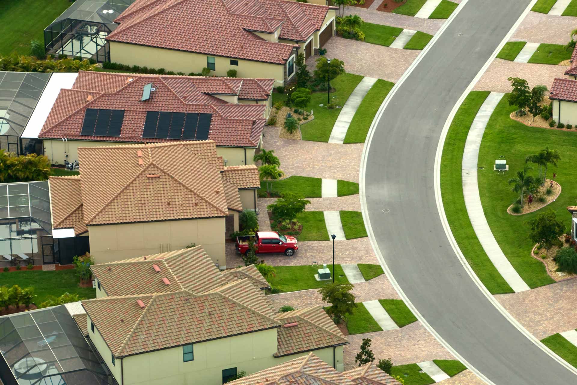 Residential neighborhood with curved road, tan houses, green lawns and solar panels.