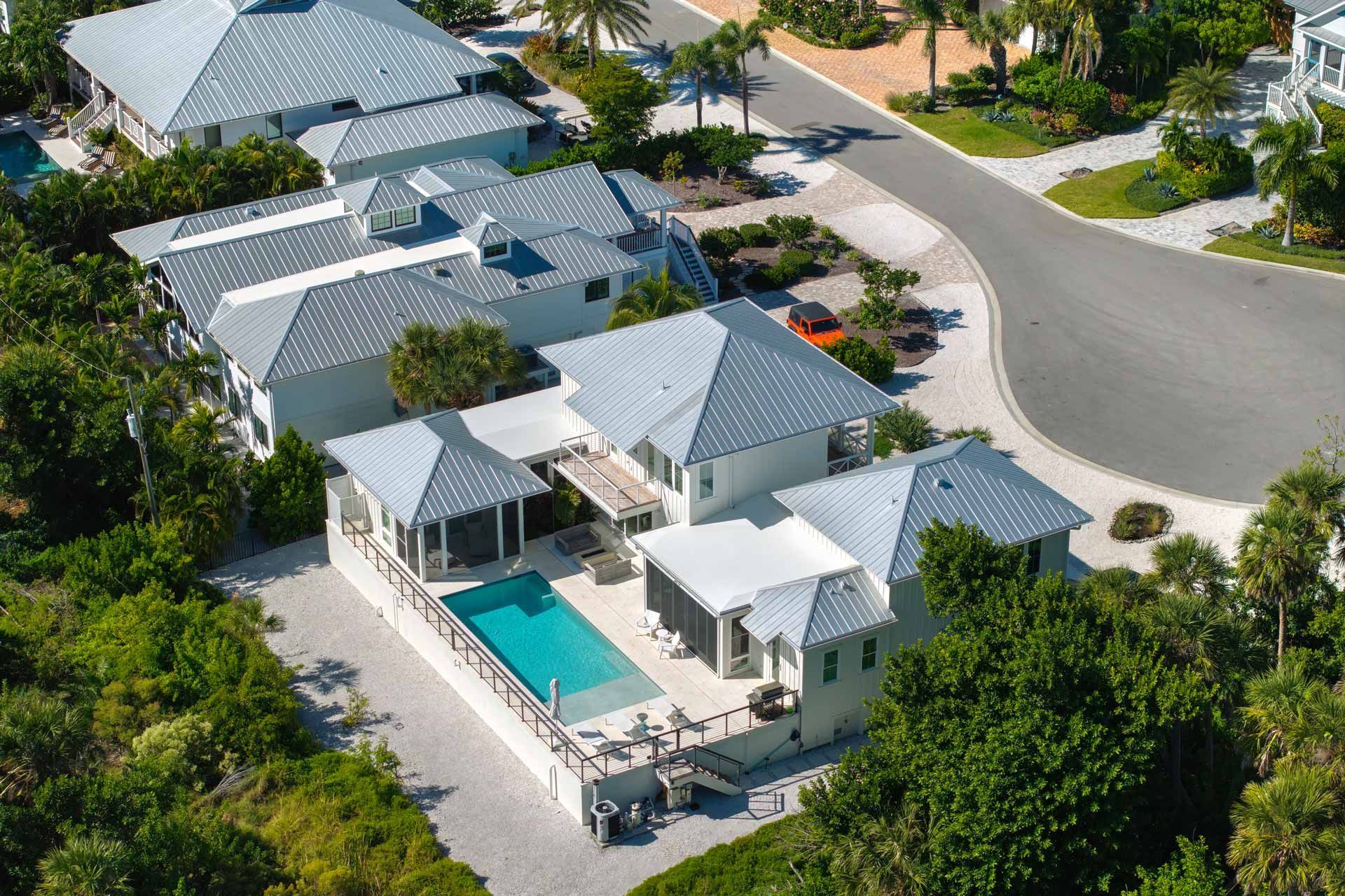 Aerial view of white houses with silver roofs, a swimming pool, and a winding road.