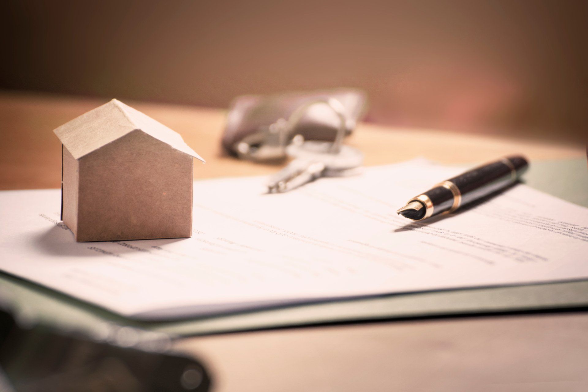 A small wooden house is sitting on top of a piece of paper next to a pen and keys.