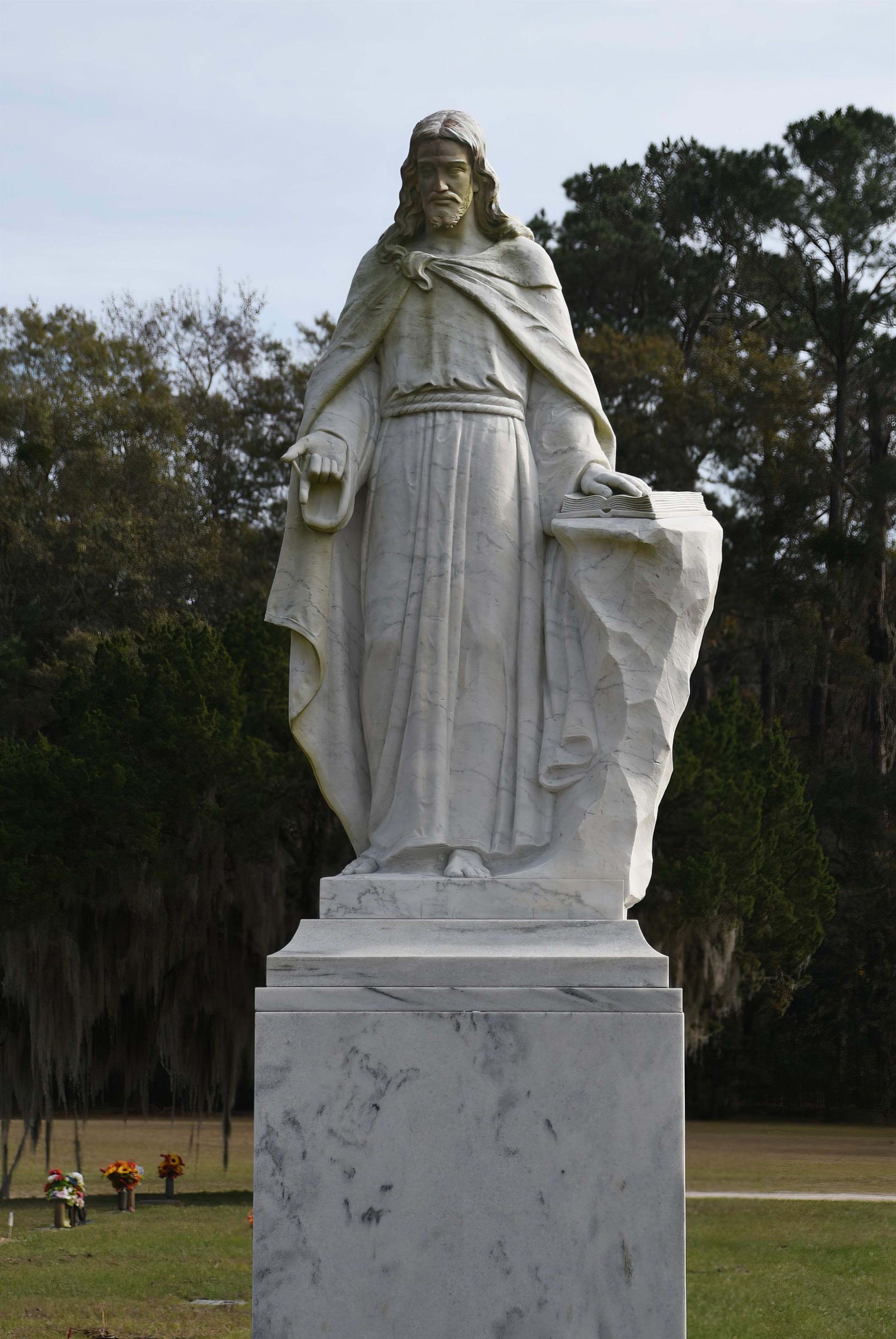 A statue of jesus in a cemetery with trees in the background