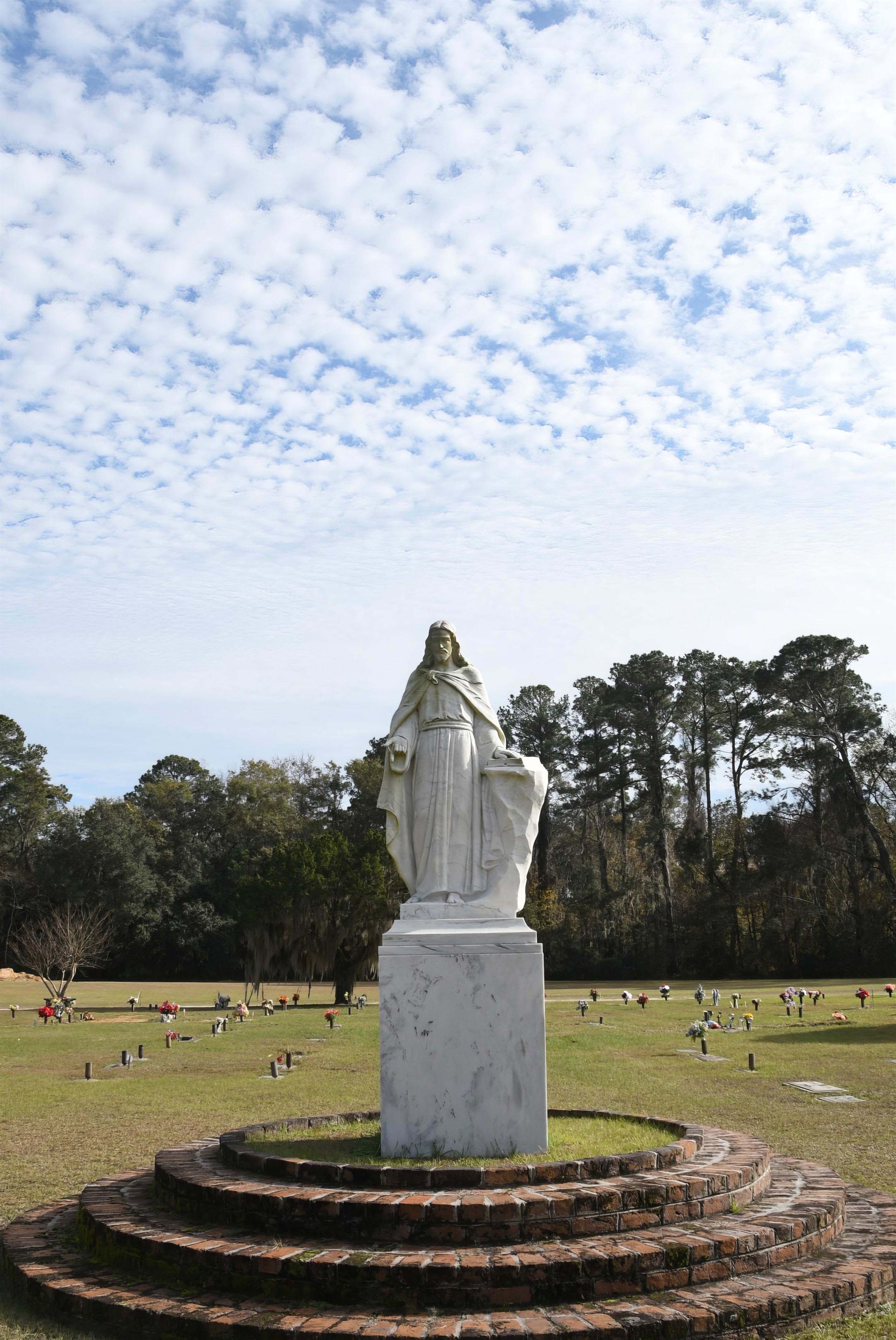 There is a statue of jesus in the middle of a cemetery.
