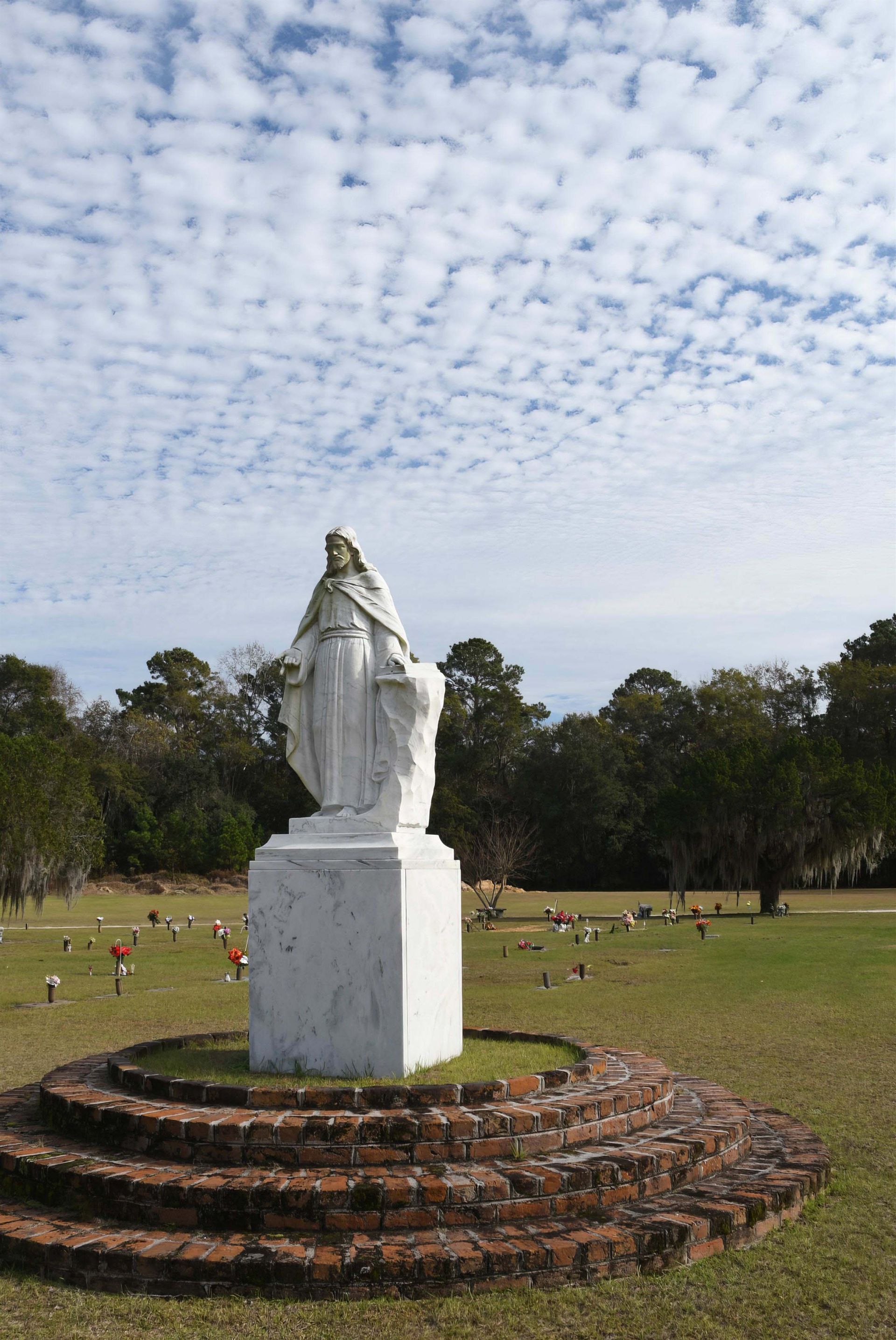 There is a statue of jesus in the middle of a cemetery.