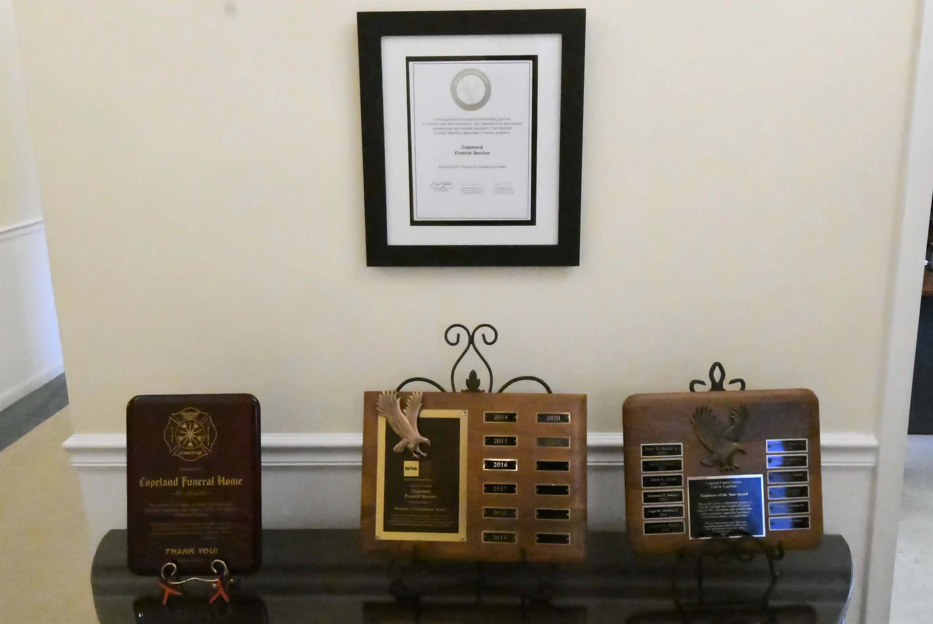 Three plaques are sitting on a table under a framed certificate