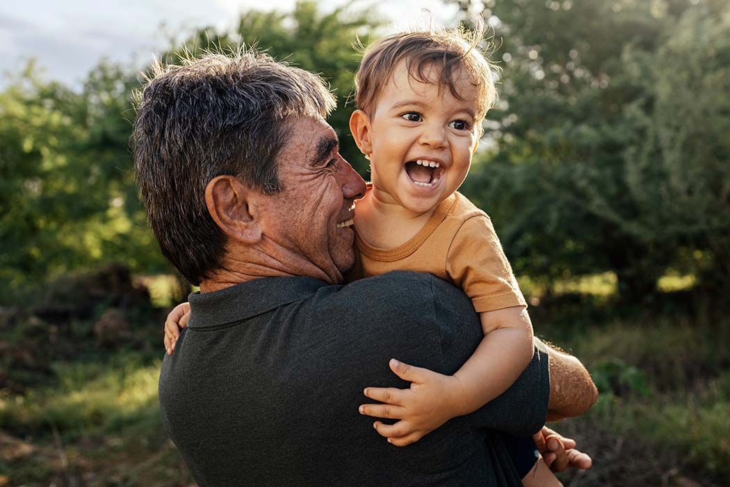 A man is holding a baby on his shoulders in a field.
