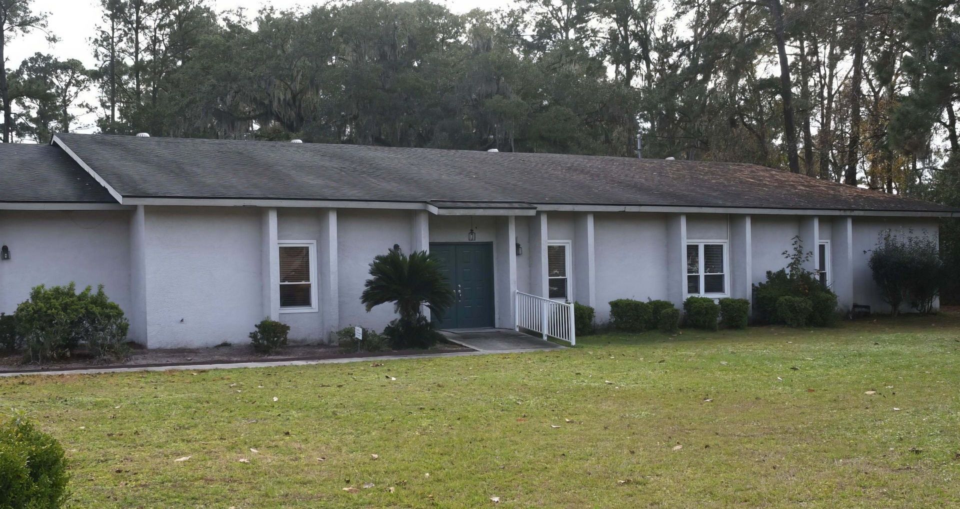 A large white house with a green door is surrounded by trees