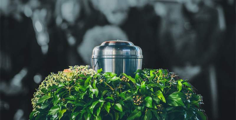 A metal urn is sitting on top of a green bush.