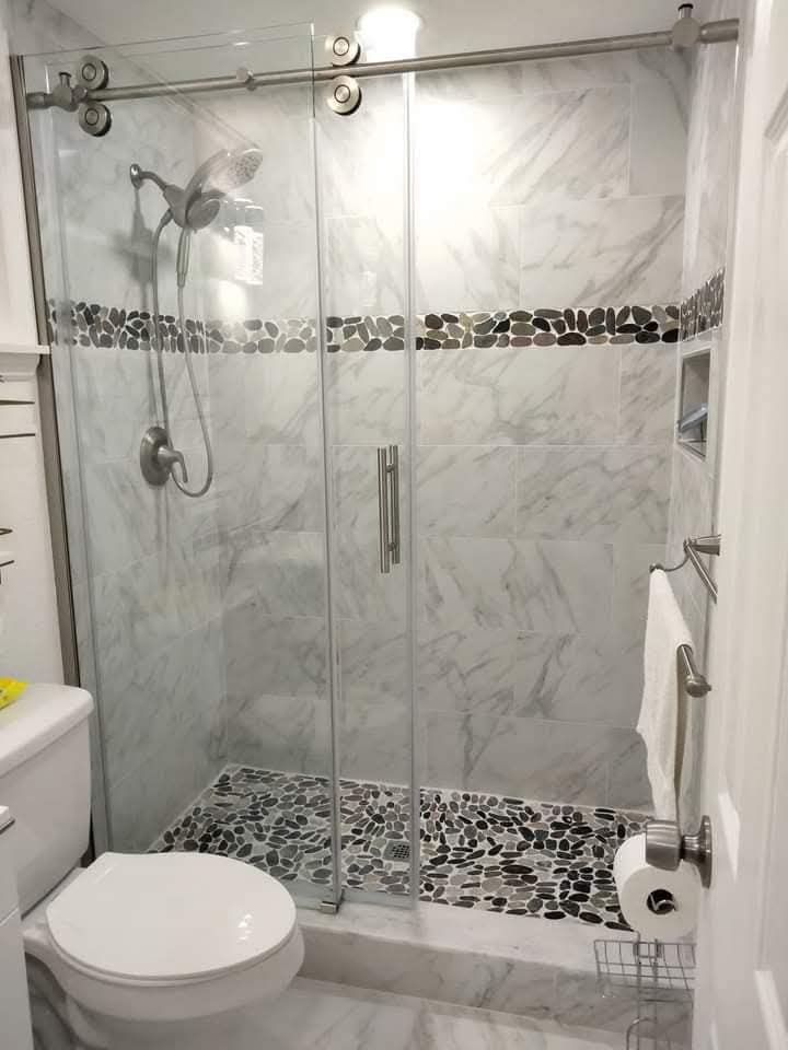 A modern bathroom with a glass shower, marble tile, and a pebble-stone shower floor.