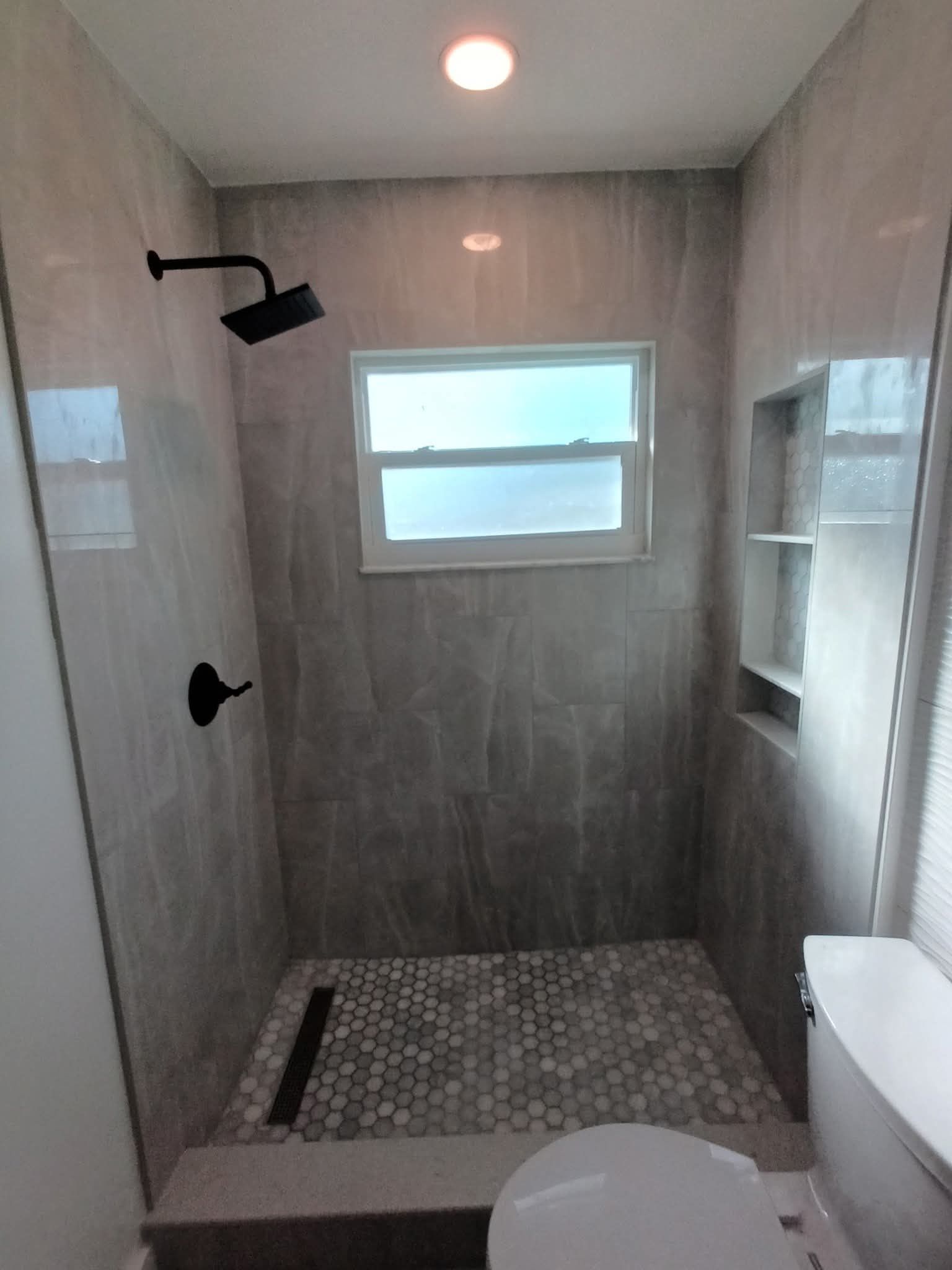 Gray tiled shower with black fixtures, small window, and mosaic floor.
