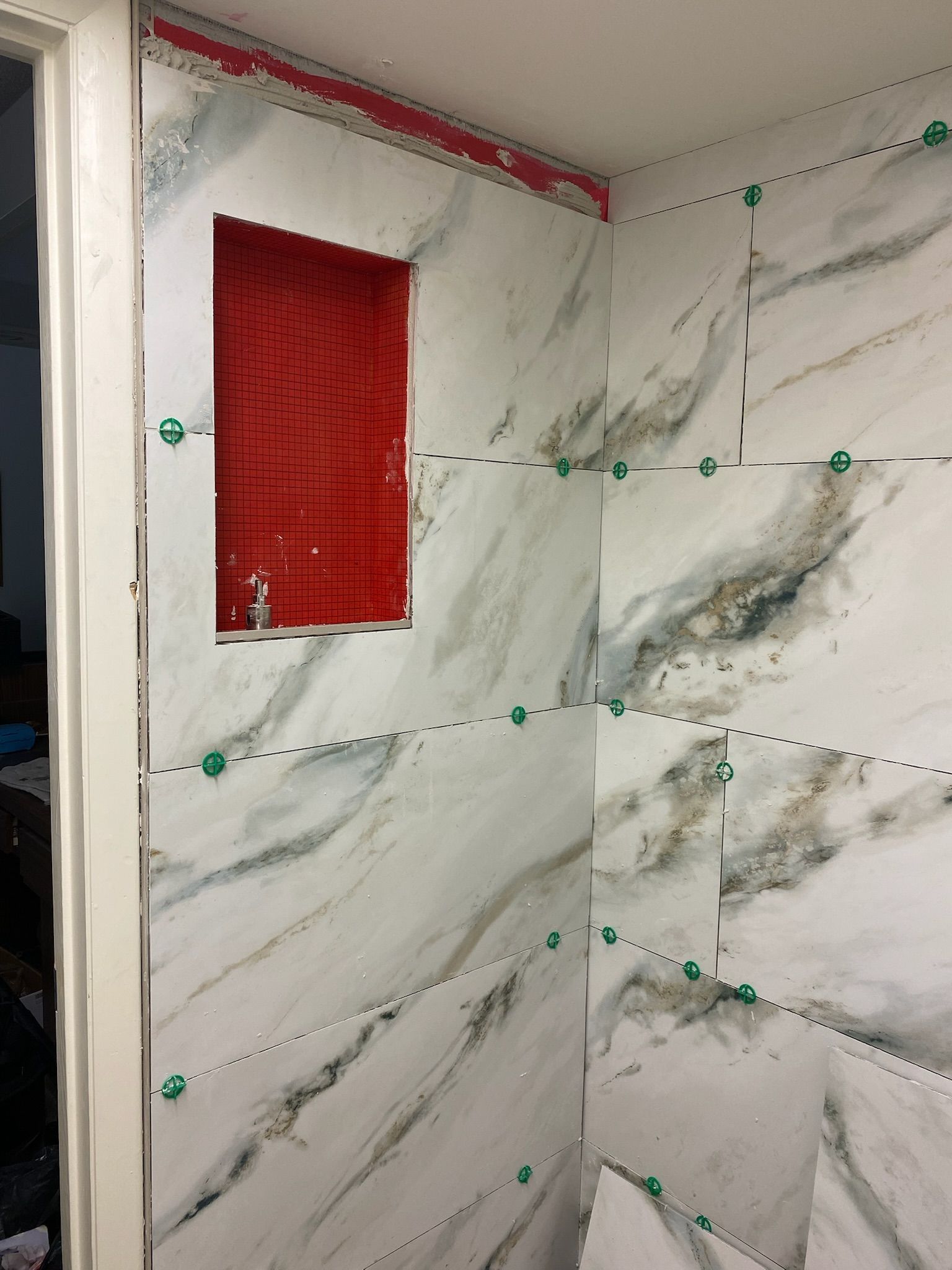A bathroom wall with marble tiles and a red niche.
