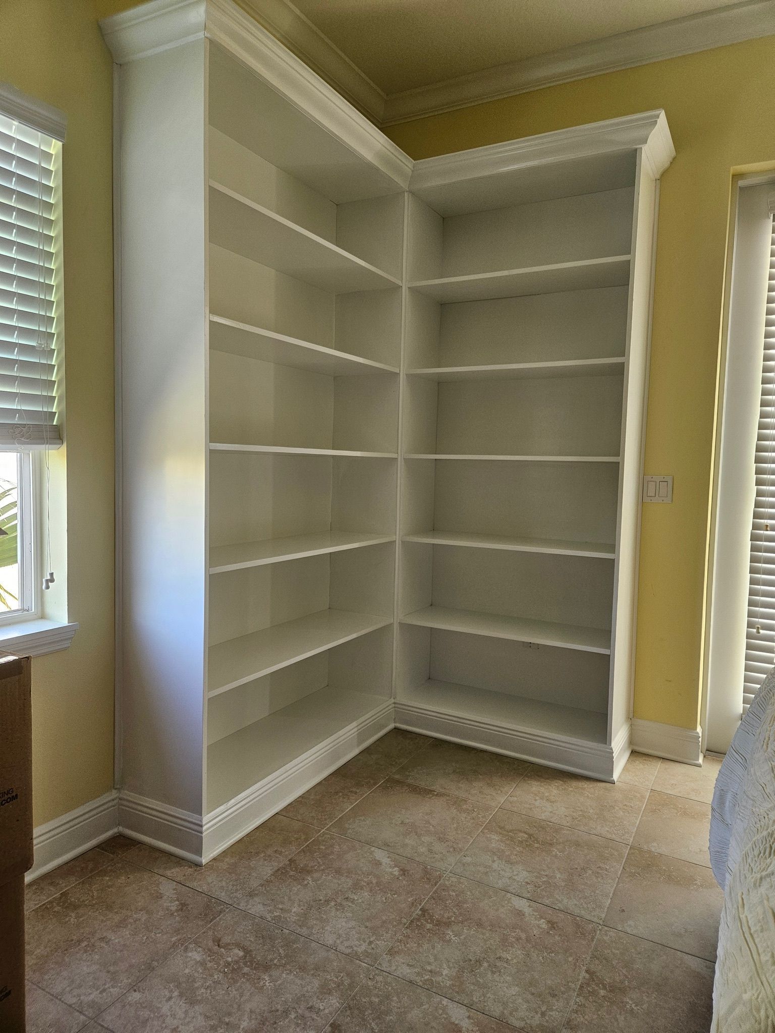 A room with a corner bookshelf and a window
