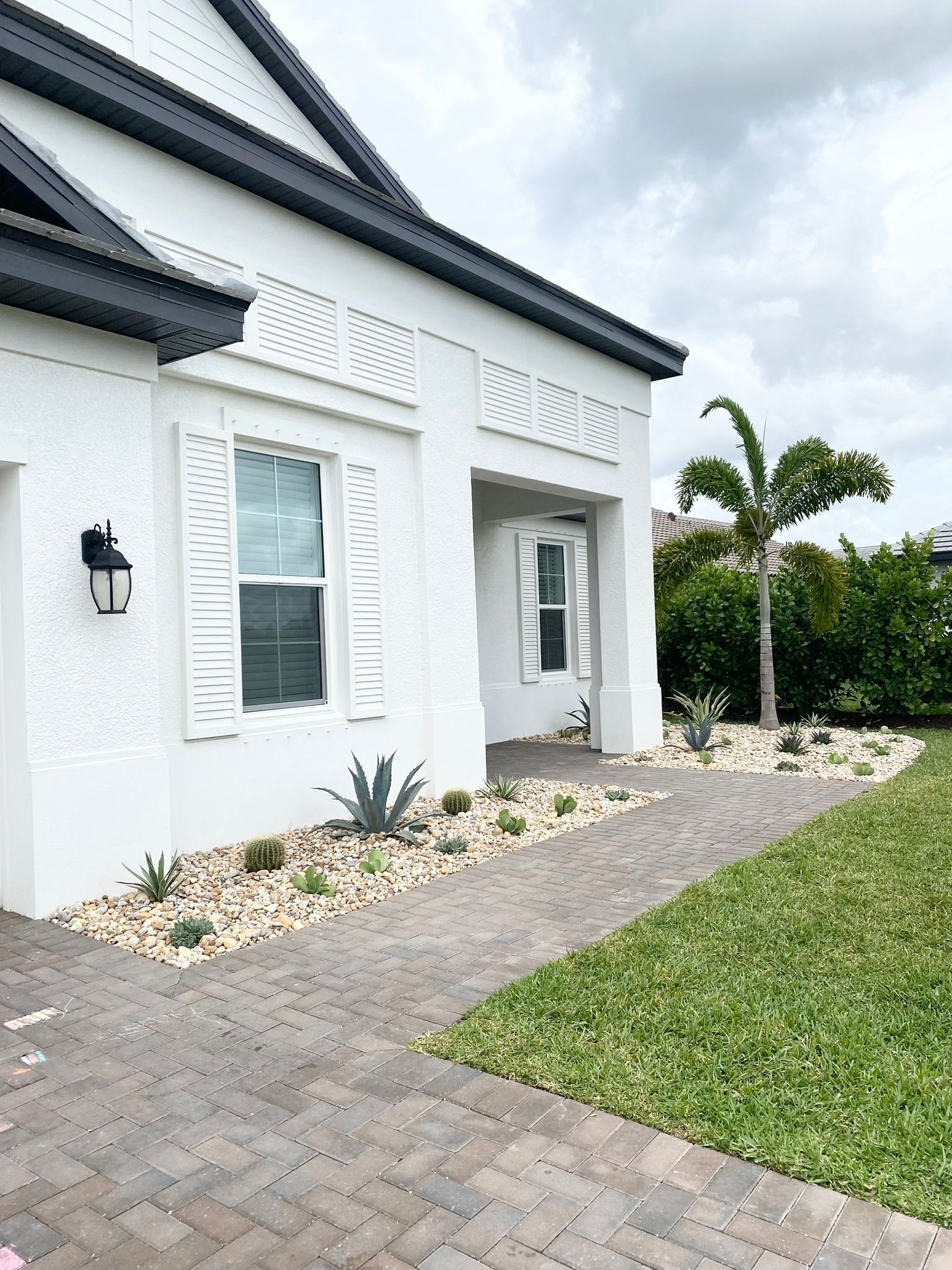 A white house with a black roof and a brick walkway leading to it.