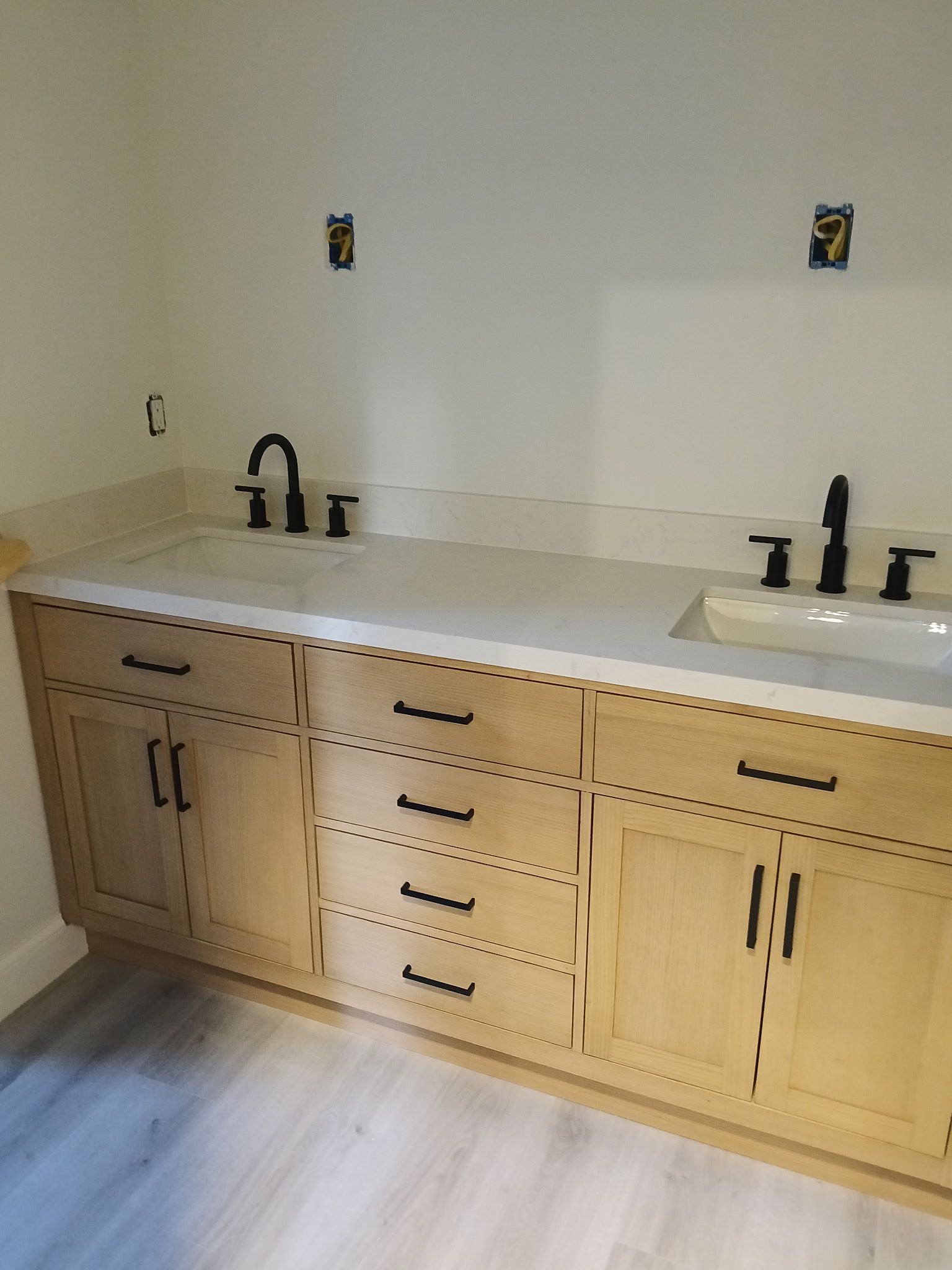 Bathroom vanity with light wood cabinets, black fixtures, and a white countertop.