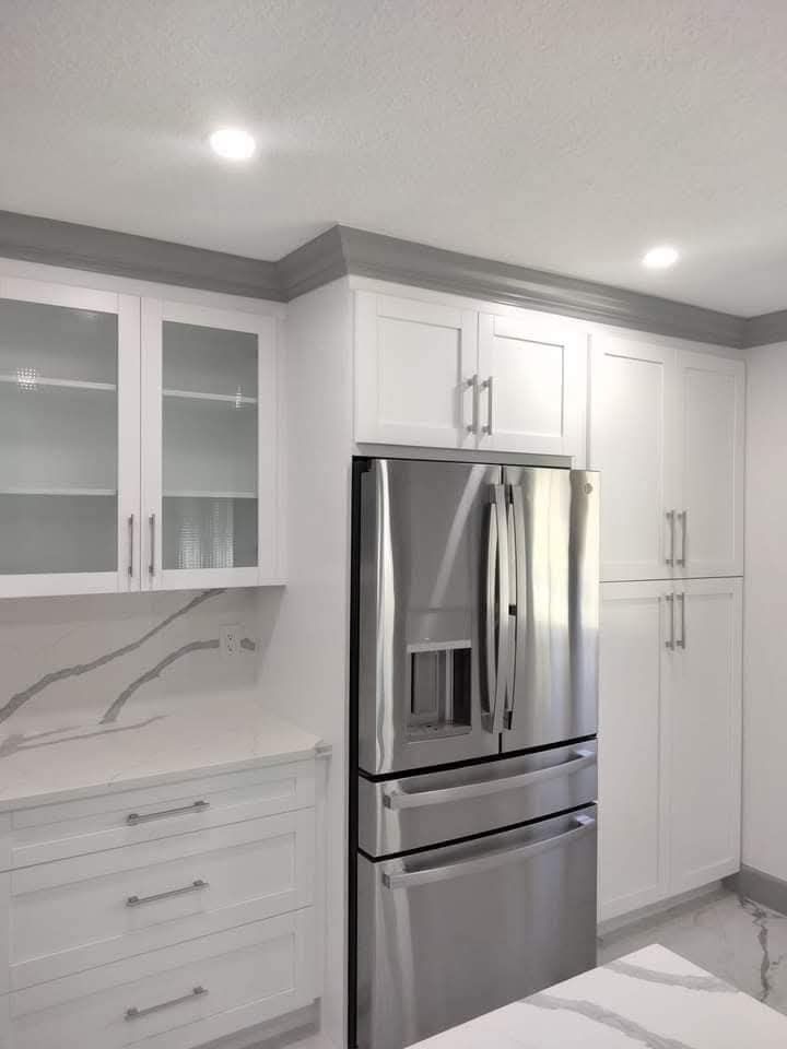 White kitchen cabinets with a stainless steel refrigerator and a grey crown molding.
