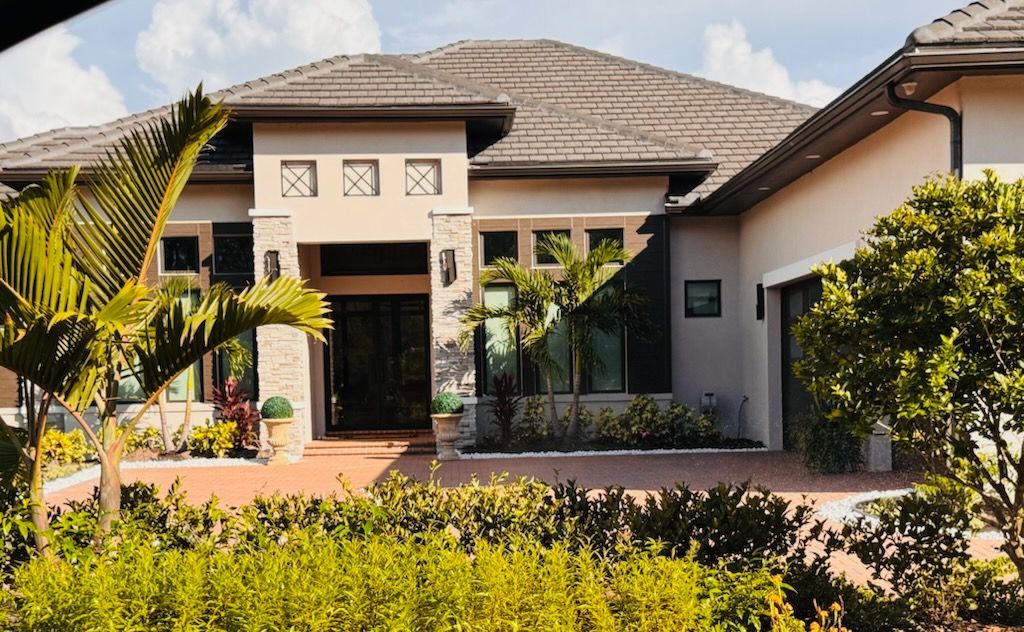 Beige and gray luxury home with a tiled roof and lush landscaping.