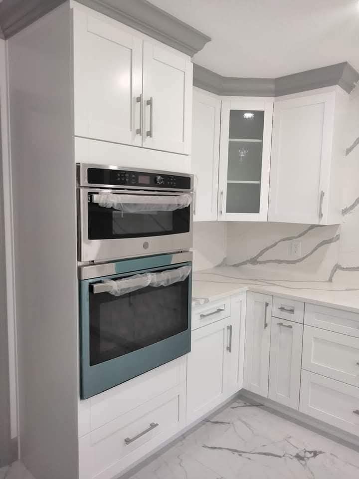 White kitchen cabinets with built-in stainless steel ovens and a marble countertop.