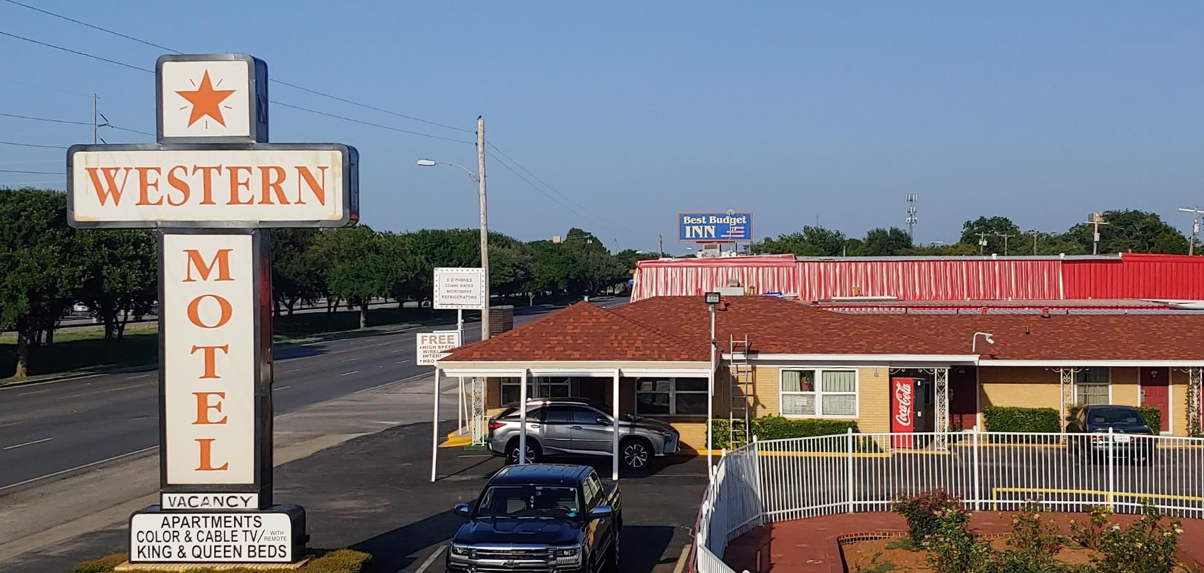Western Motel roadside sign beside a red-roofed motel with parked cars under a clear blue sky
