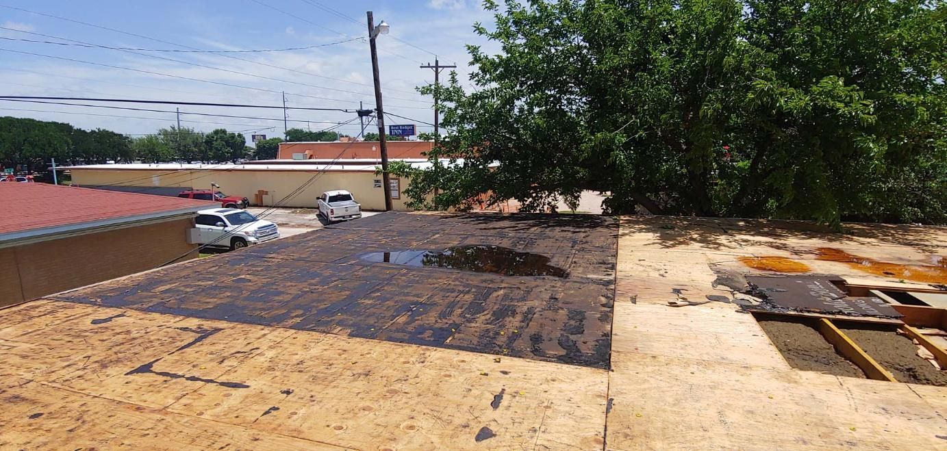 Rooftop with dark gravel, tan roofing, nearby trees, and parked cars under a bright sky