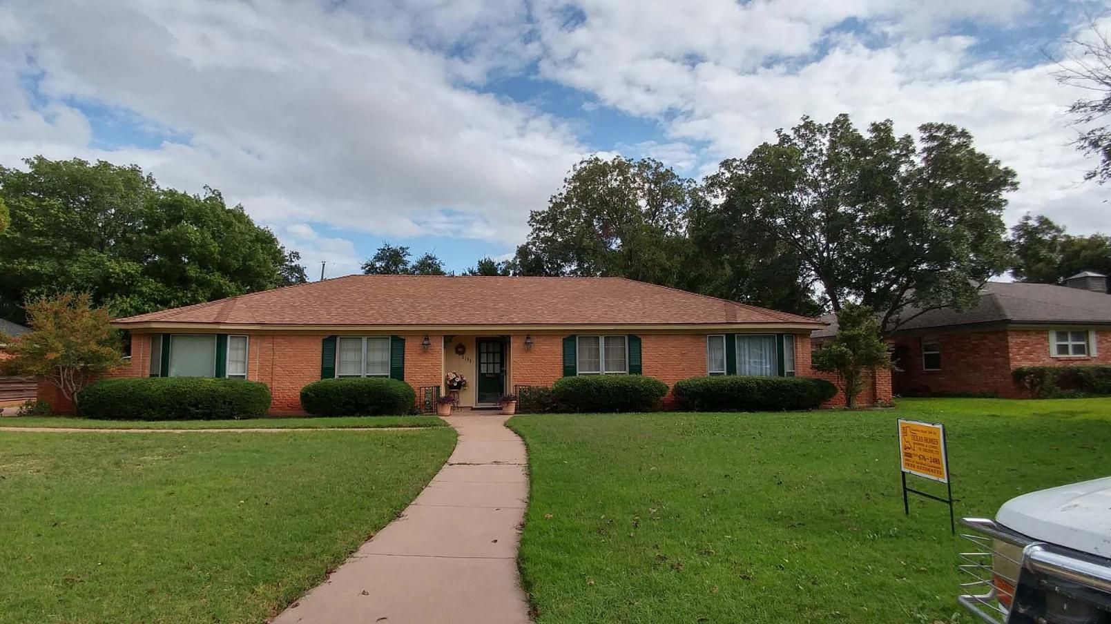 Single-story brick house with a front walkway, green lawn, and cloudy sky