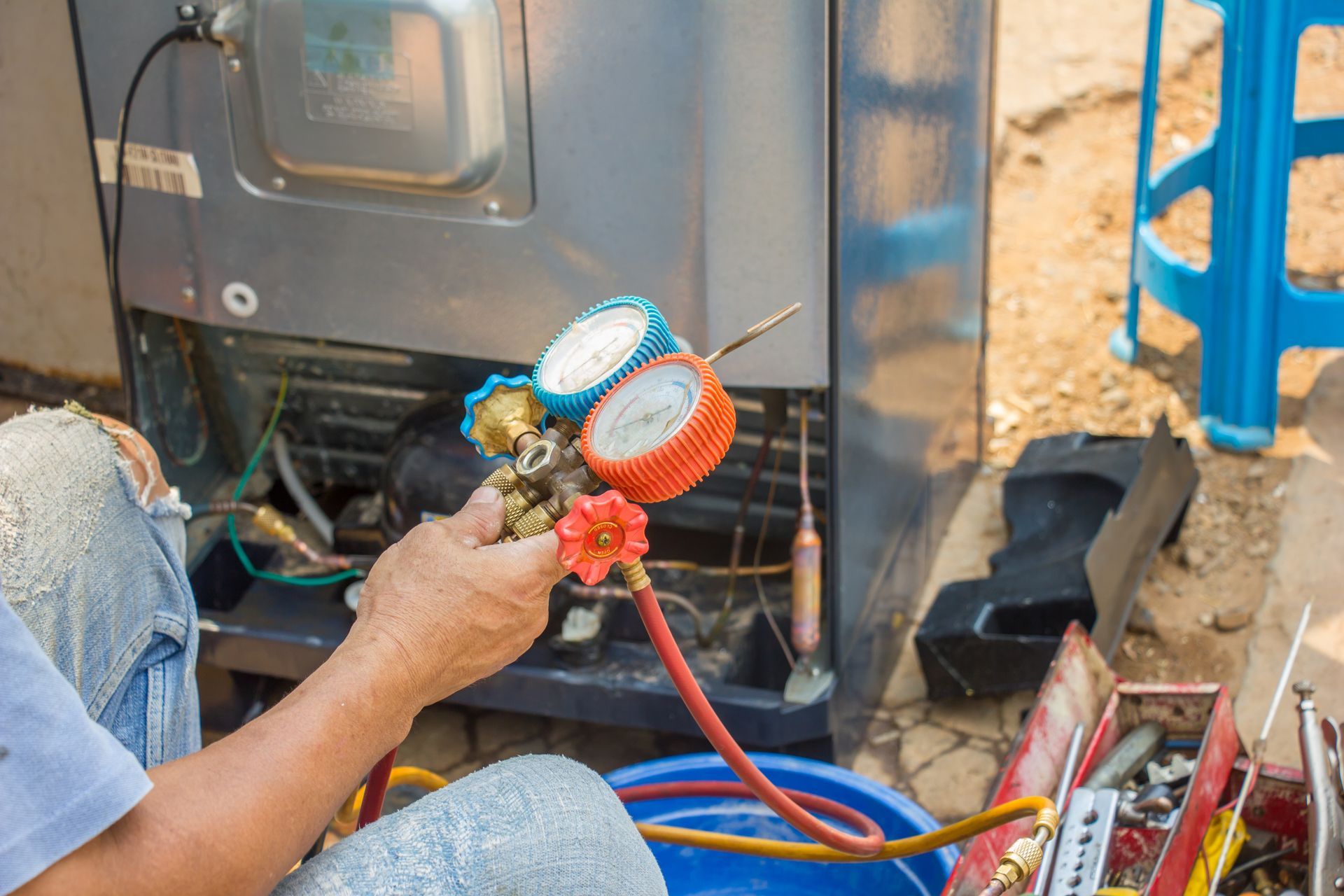 Technician using a pressure gauge to repair a refrigerator at a maintenance shop.